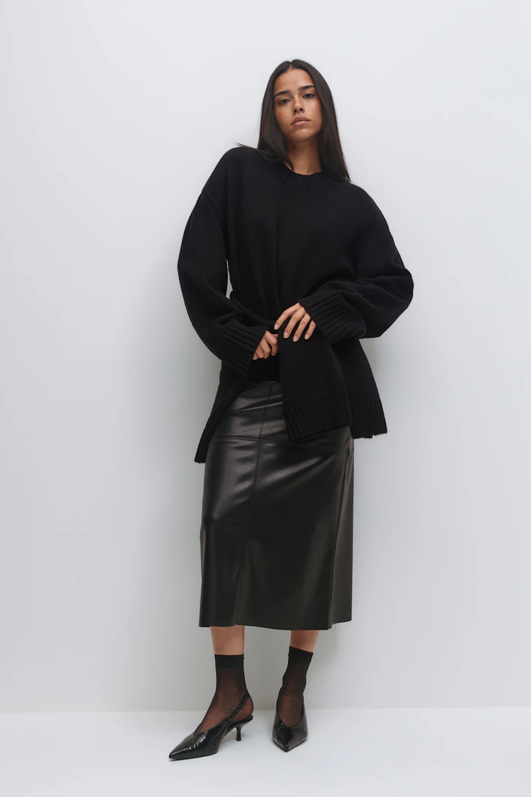 Schwarzer Pullover mit übergroßem Rundhalsausschnitt und gerippten Bündchen und Saum, schwarzer Midirock aus Leder, schwarze durchsichtige Söckchen und spitze schwarze Slingback-Kitten-Heels.