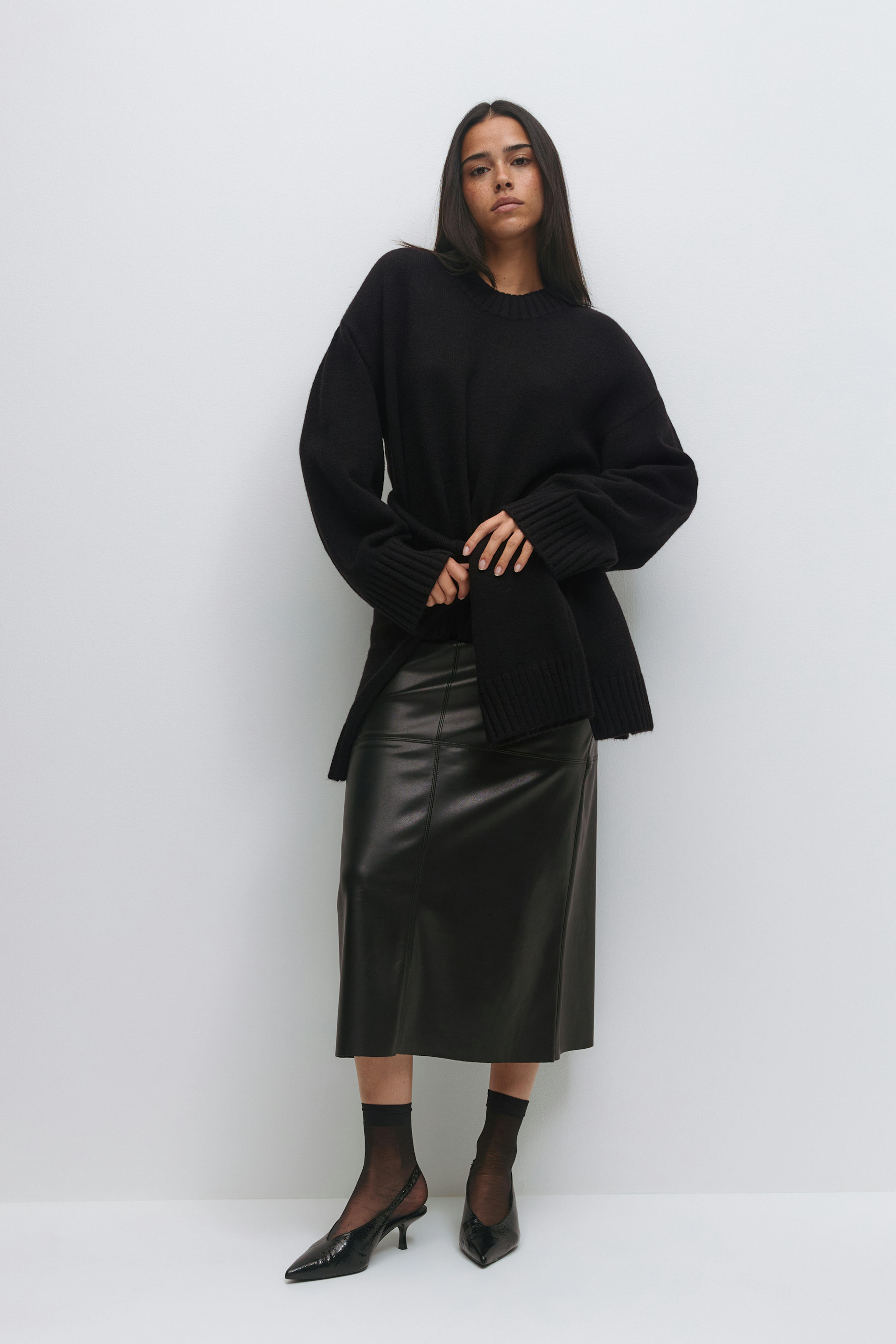 Oversized black crewneck sweater with ribbed cuffs and hem, black leather midi skirt, sheer black ankle socks and pointed black slingback kitten heels.
