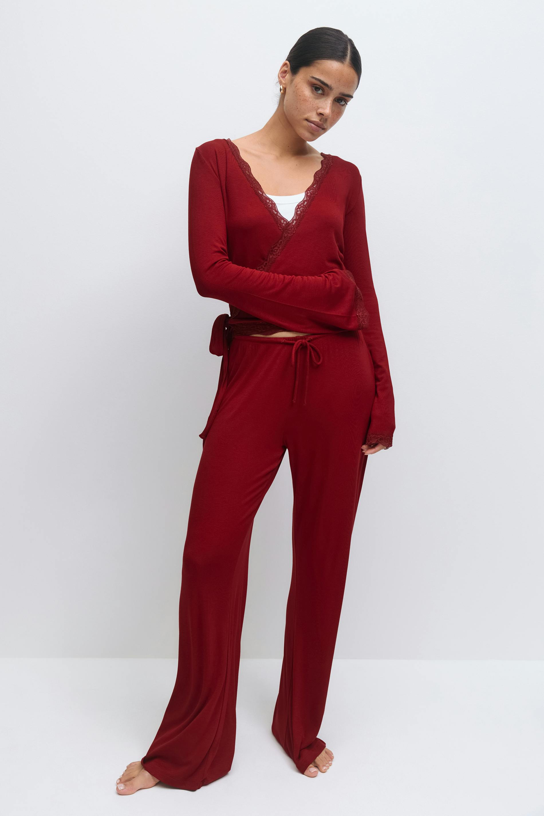 Burgundy long-sleeve lace-trim wrap top layered over a white camisole, paired with matching wide-leg drawstring trousers.