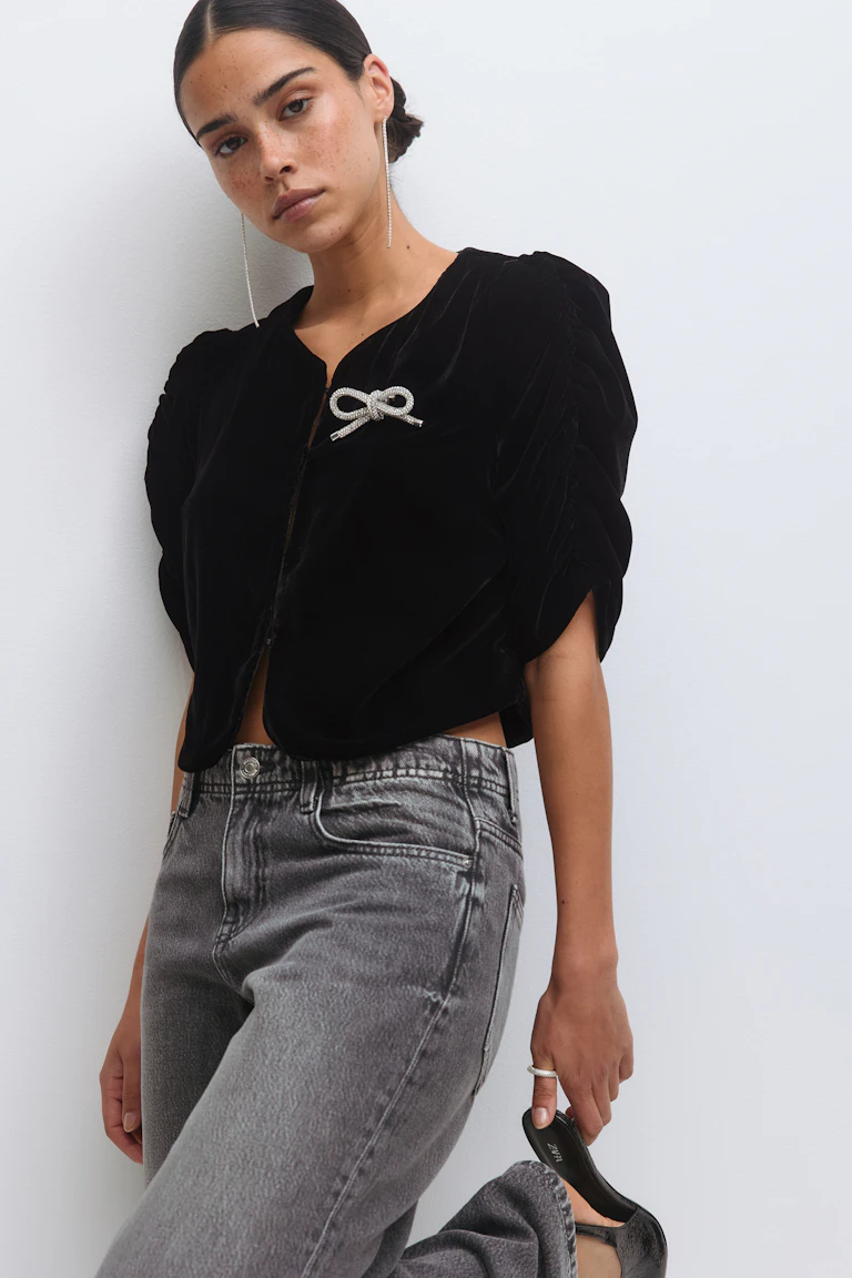 Musta samettipusero, jossa on röyhelöhihat ja kristallirusetti rinnassa; pitkät kristallikorvakorut; korkeavyötäröiset haalistuneet harmaat farkut; kädessä mustat korkokengät ja ohut hopeinen sormus.