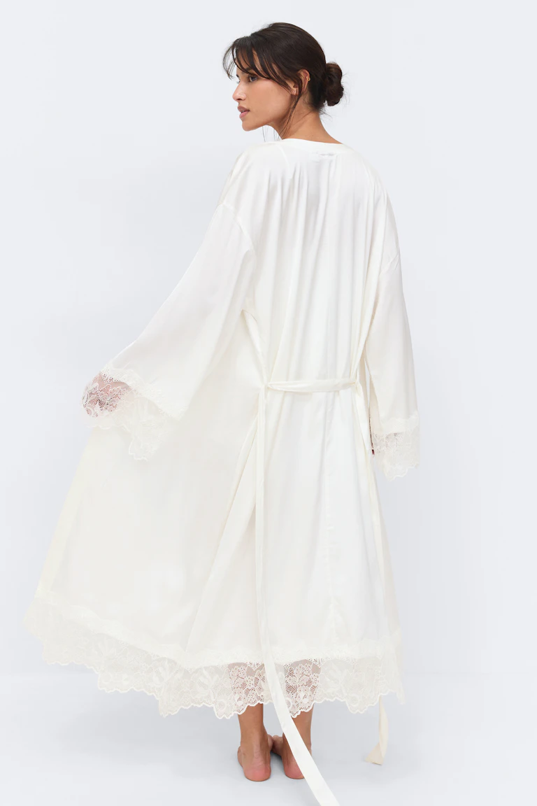 Knöchellange Robe aus elfenbeinfarbenem Satin mit weiten Ärmeln, Spitzenbesatz an Manschetten und Saum und einem Gürtel zum Binden in der Taille.