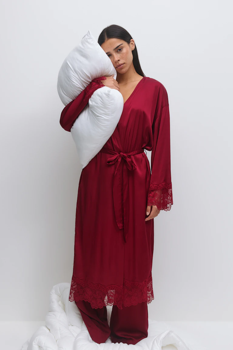 Deep burgundy satin long robe with V-neck, lace-trimmed cuffs and hem, self-tie waist belt, paired with matching satin wide-leg trousers.