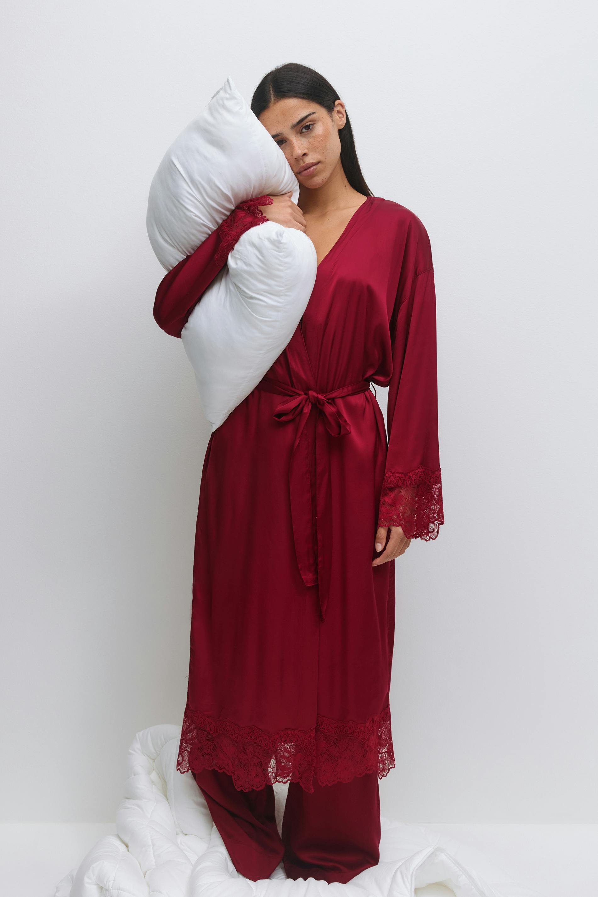 Dyp burgunderfarget lang kappe i sateng med V-utringning, blondekant i mansjetter og nederkant, selvbindende belte i livet, kombinert med matchende bukser i sateng med vide ben.