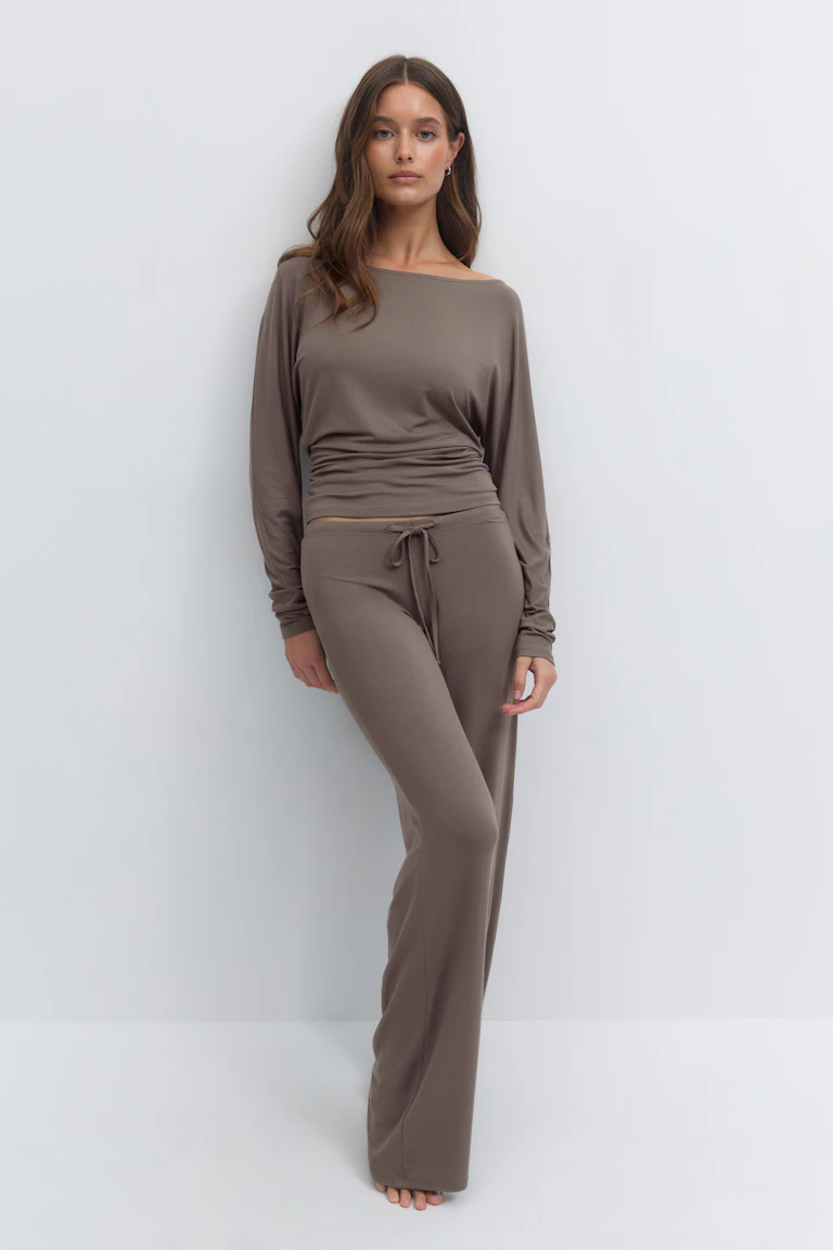 Das Modell trägt ein passendes taupefarbenes langärmeliges Oberteil mit geraffter Taille und eine dazu passende Hose mit weitem Bein und hohem Bund.