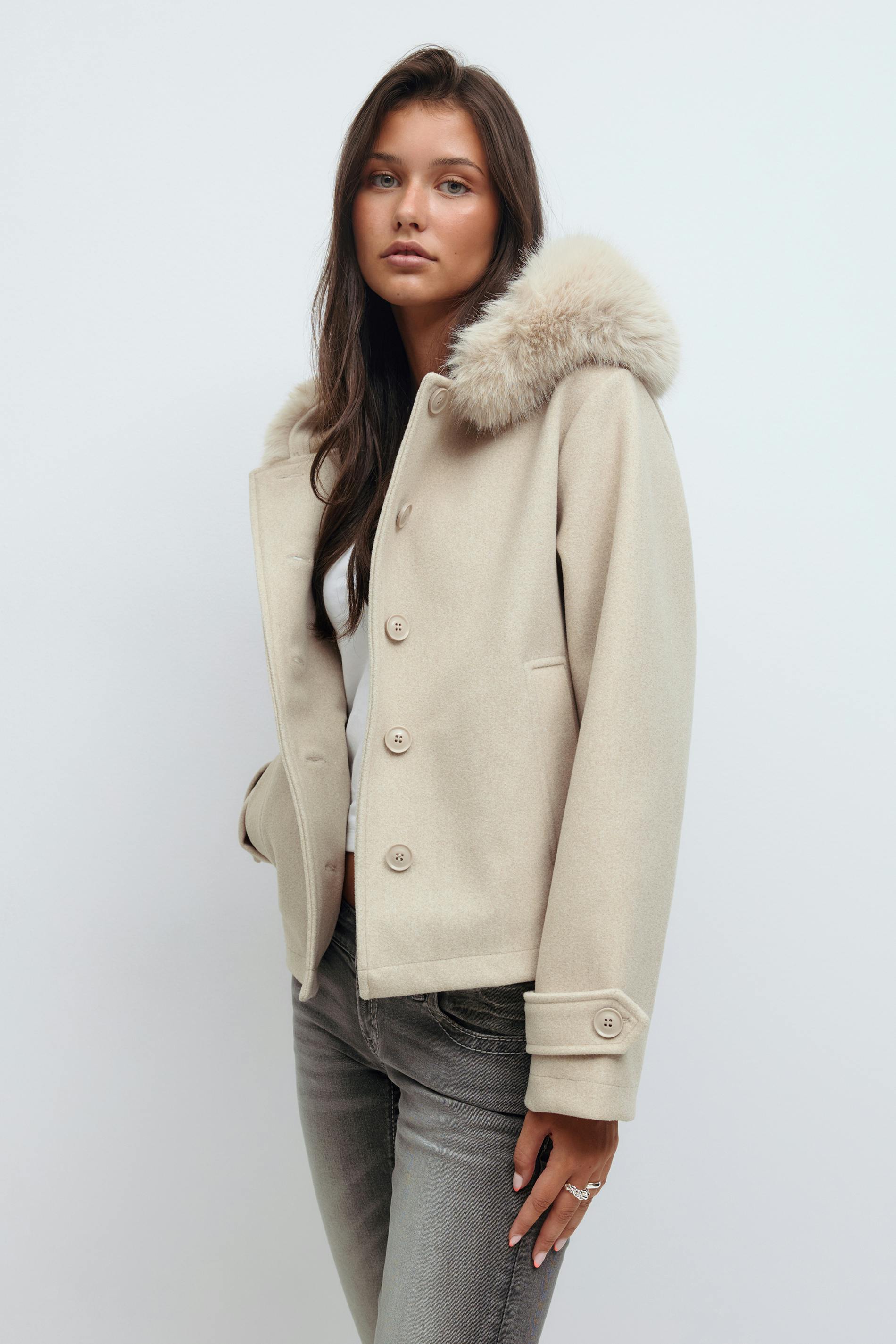 Beige wool button-front jacket with fur-trimmed hood, welt pockets and button-tab cuffs, worn over a white top and paired with grey slim-fit jeans.