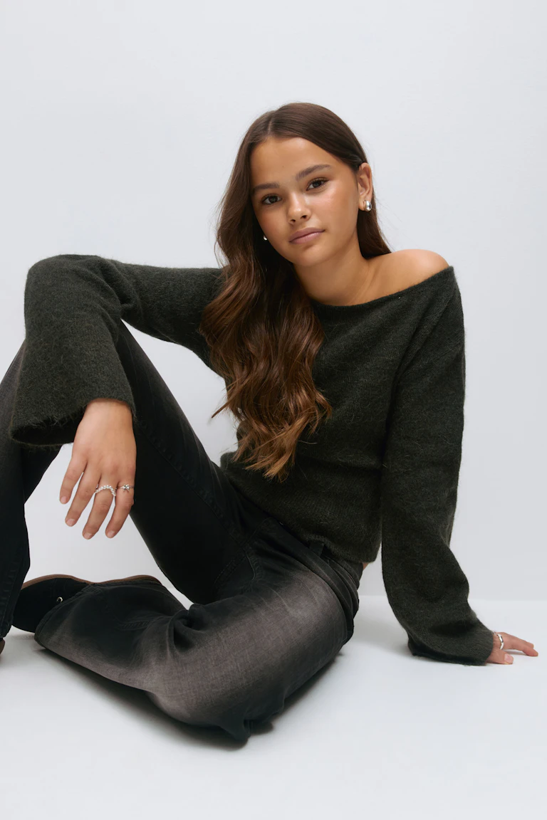 Off-the-shoulder dark charcoal mohair sweater, faded black jeans, silver hoop earrings and multiple silver rings.