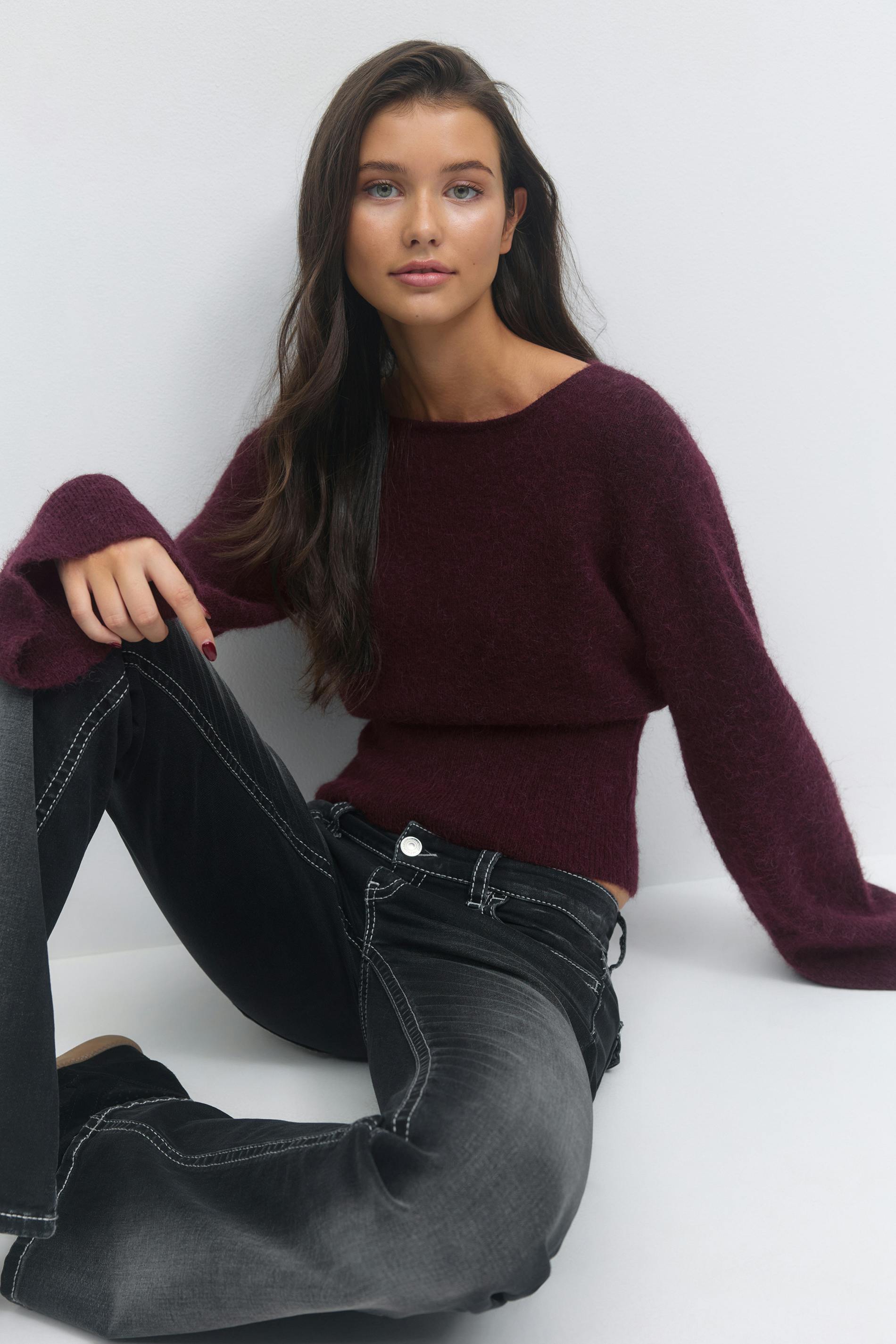 Langärmeliger Pullover mit Bootsausschnitt in tiefem Burgunderrot und verwaschenen schwarzen Jeans mit weißen Kontrastnähten.