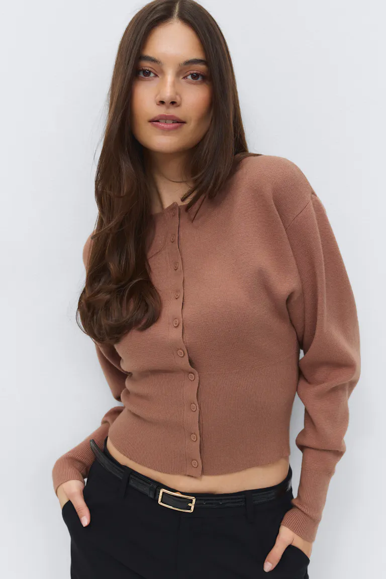 Braune, geknöpfte Strickjacke mit langen Ärmeln und geripptem Saum und Manschetten, kombiniert mit einer schwarzen, taillierten Hose und einem schmalen, schwarzen Gürtel mit einer goldenen, rechteckigen Schnalle.