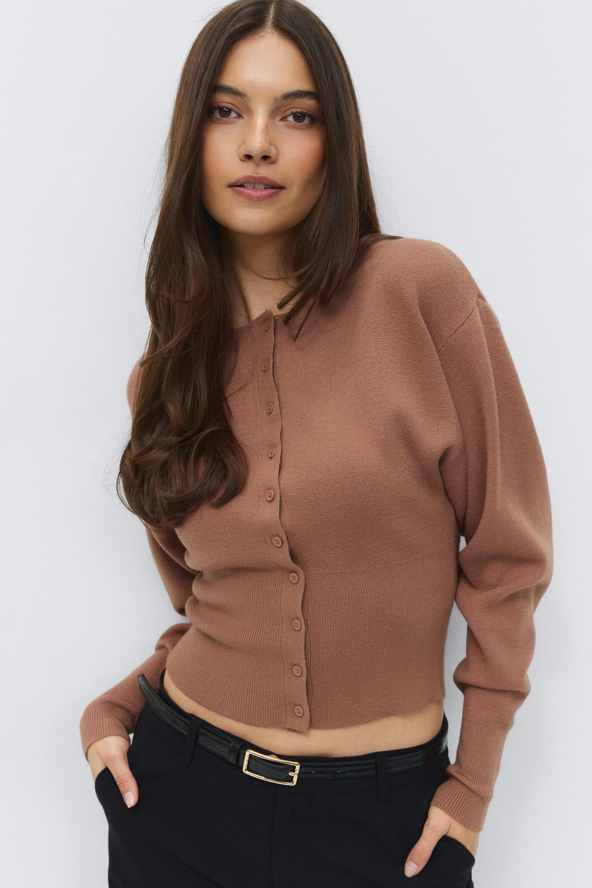 Brown cropped button-front cardigan with long sleeves and ribbed hem and cuffs, paired with black tailored trousers and a slim black belt with a gold rectangular buckle.