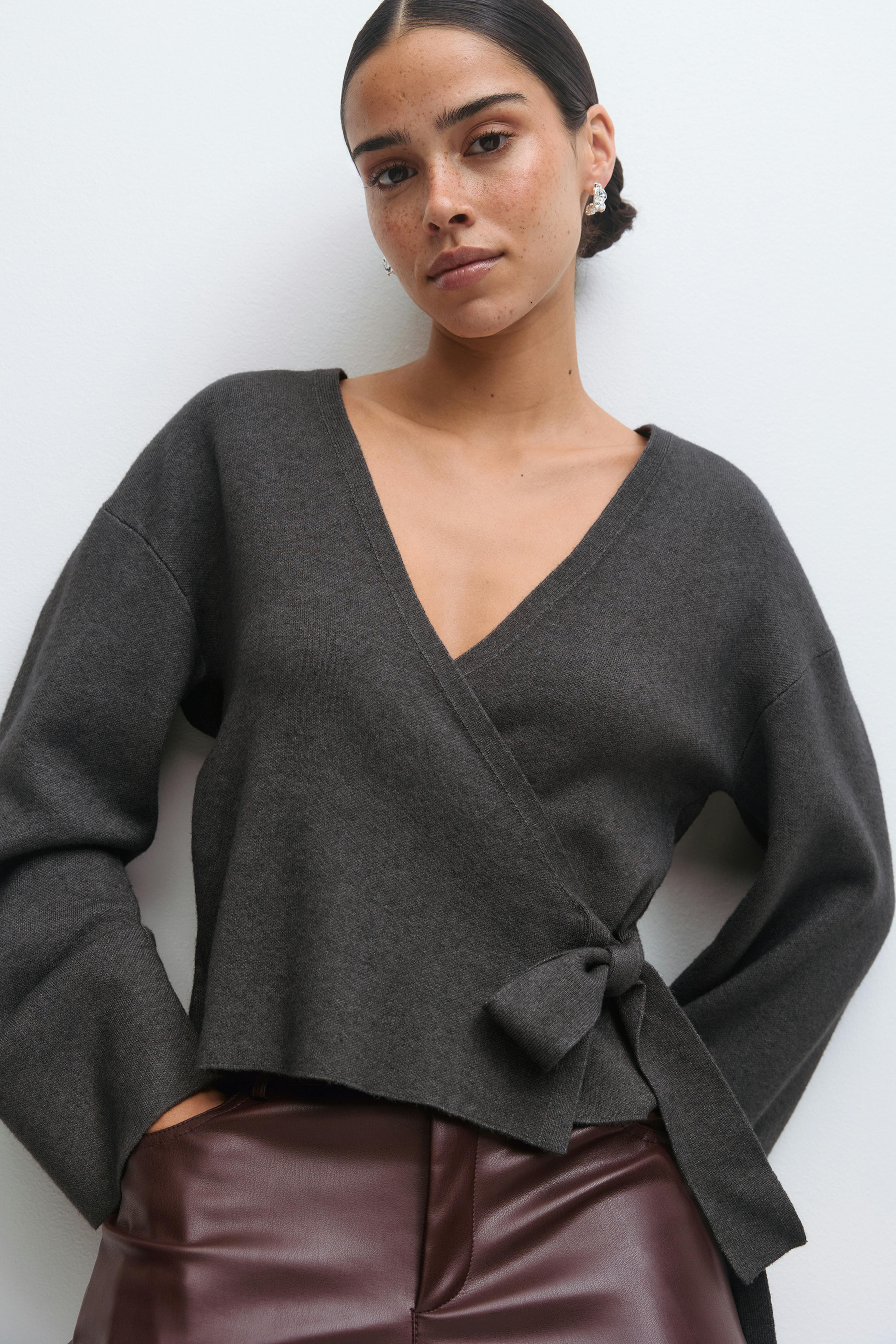 Anthrazitfarbener Wickelpullover mit V-Ausschnitt, langen Ärmeln und seitlicher Bindung, kombiniert mit einer burgunderroten Lederhose mit hoher Taille.