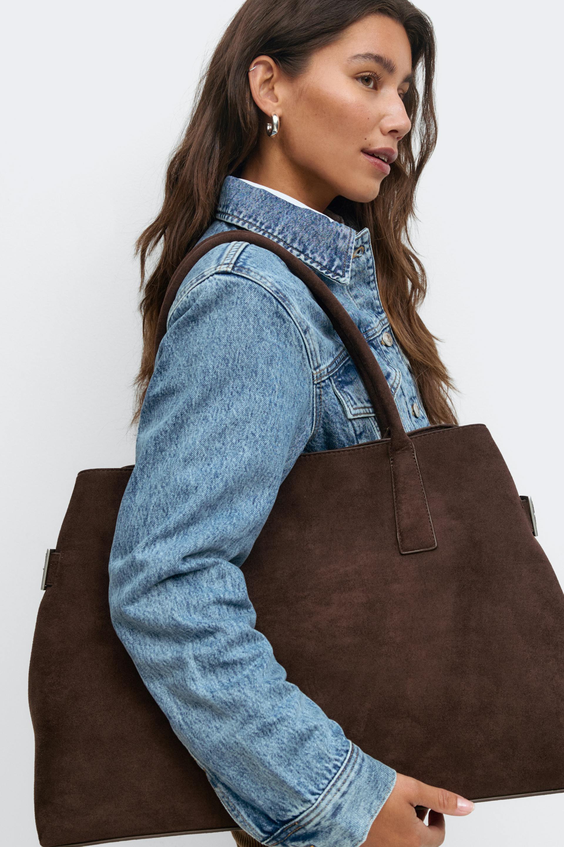 Light blue denim jacket over a white top, silver hoop earrings, and a large brown suede tote bag with shoulder straps.
