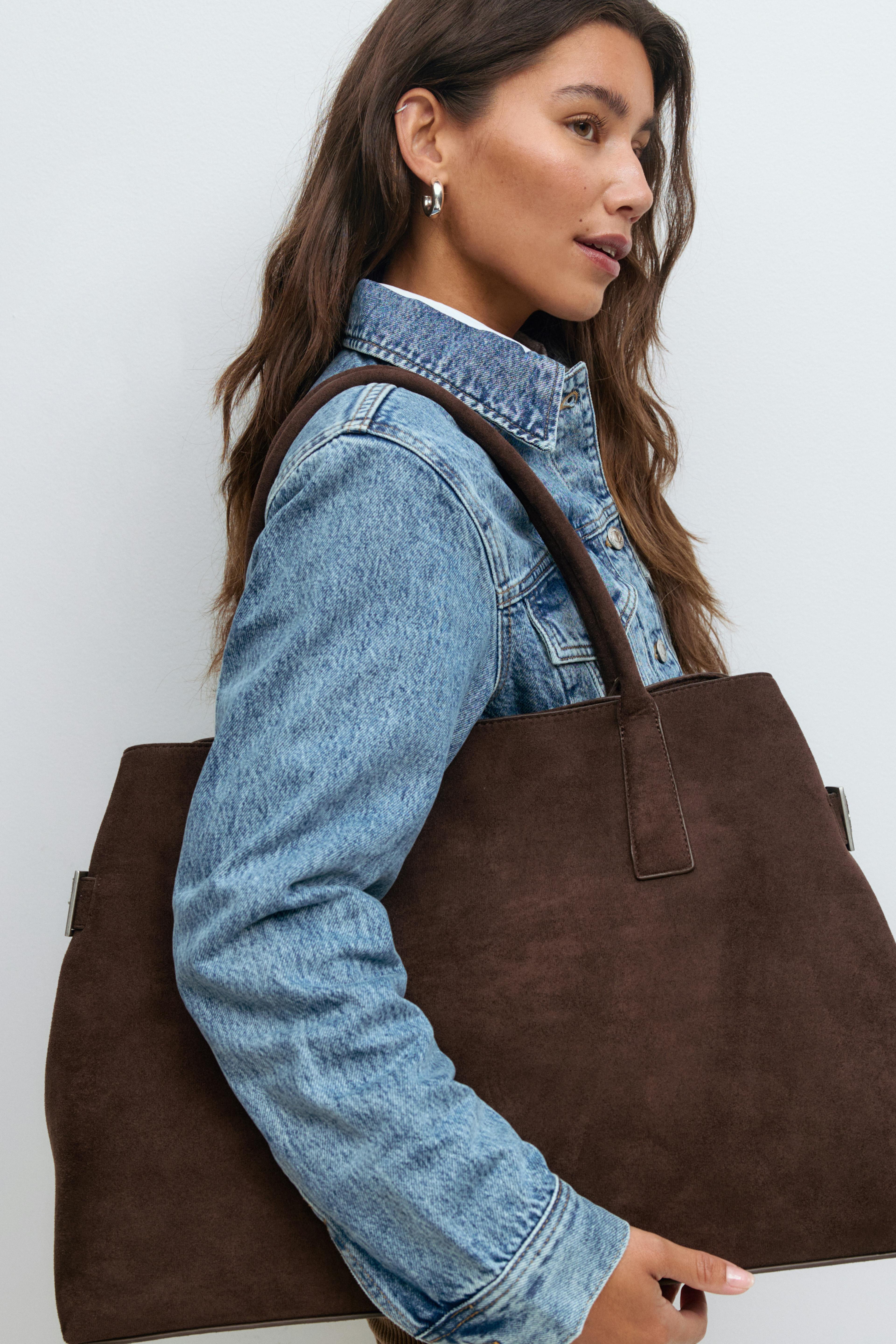 Hellblaue Jeansjacke über einem weißen Oberteil, silberne Ohrringe und eine große braune Wildleder-Tasche mit Schulterriemen.