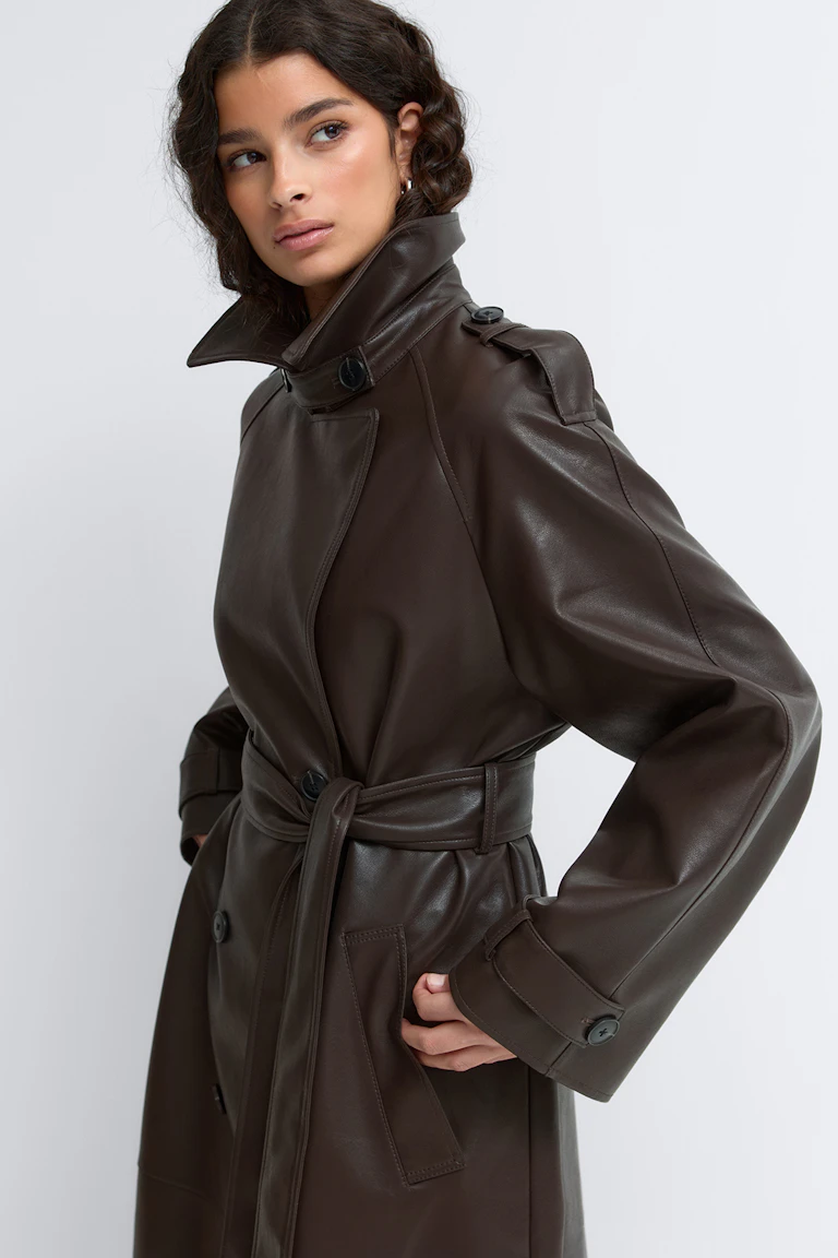 Dark brown leather trench coat with high stand collar, shoulder epaulettes, buttoned cuffs, belted waist and slanted welt pockets.
