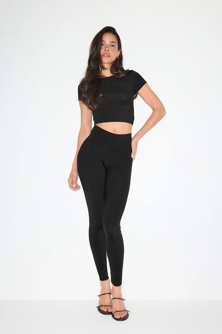 Musta lyhythihainen crop-top, yhdistettynä korkeavyötäröisiin mustiin leggingsiin ja mustiin remmisandaaleihin.