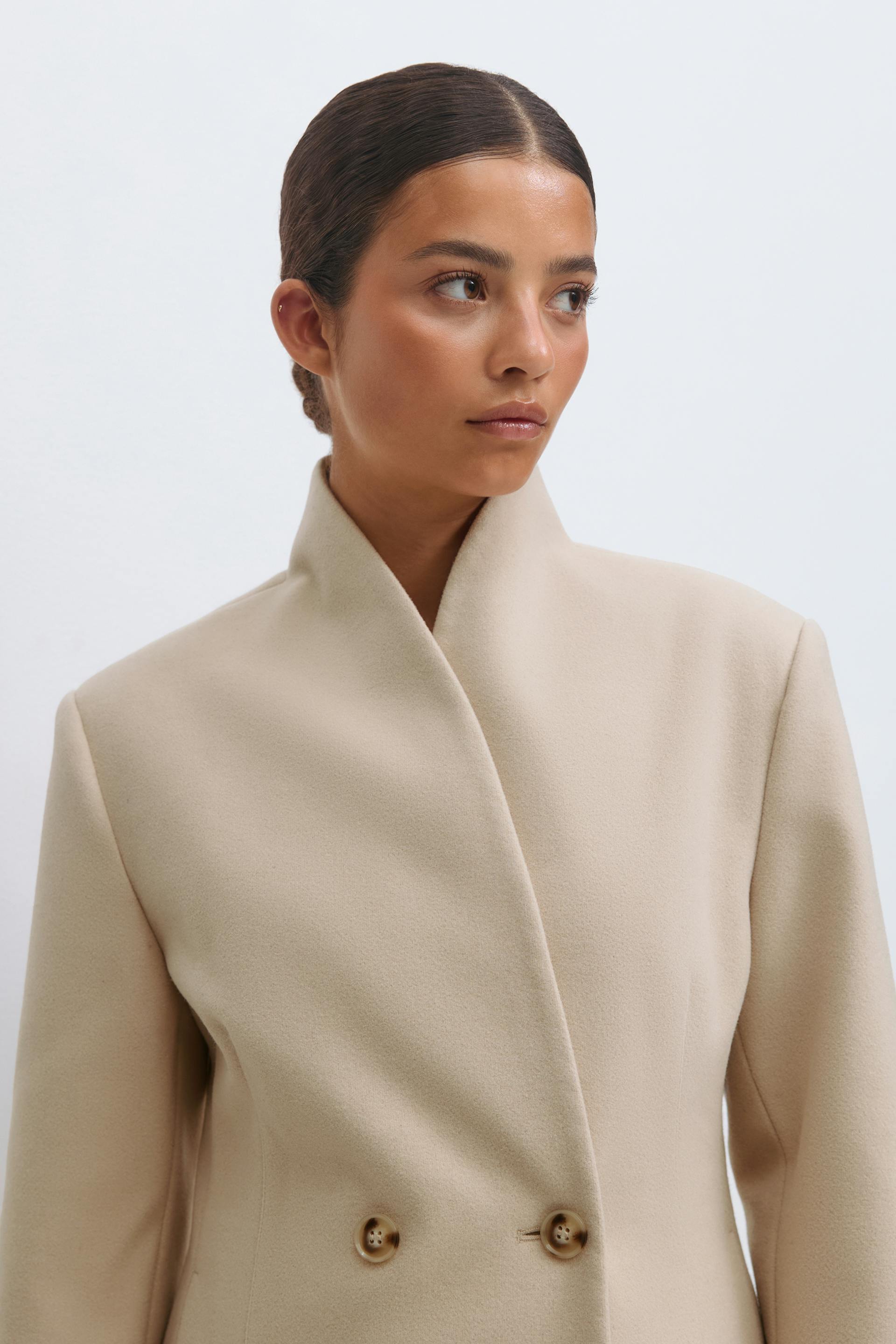 Beige double-breasted wool coat with a high stand collar and two front buttons.