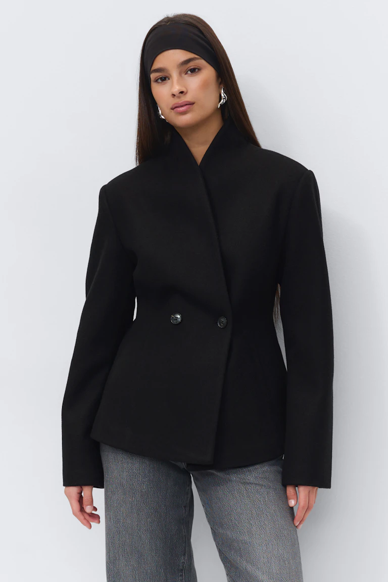 Tailored black double-breasted jacket with a high stand collar, paired with grey straight-leg jeans, a black wide headband and silver statement earrings.