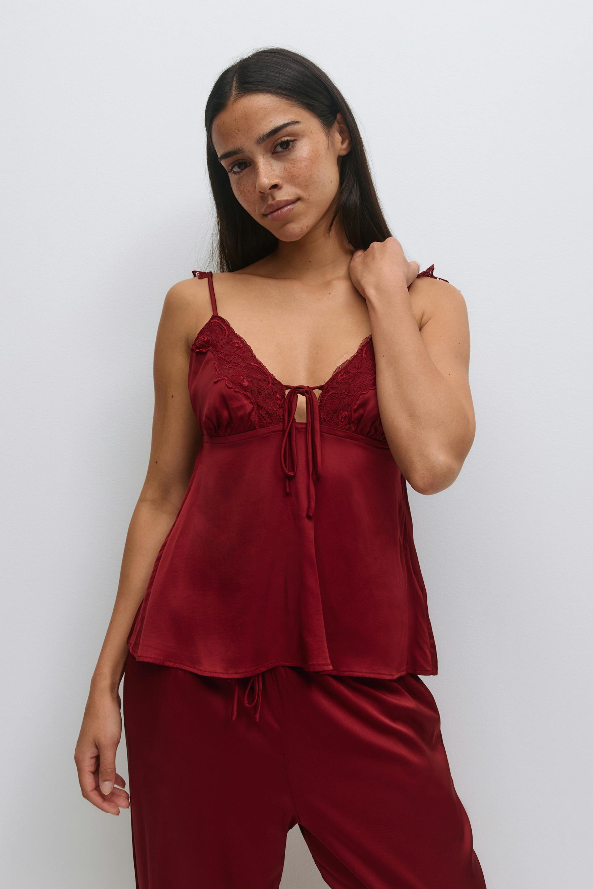 Burgundy satin camisole with lace‑trimmed cups, front tie keyhole and thin straps, paired with matching satin drawstring trousers.