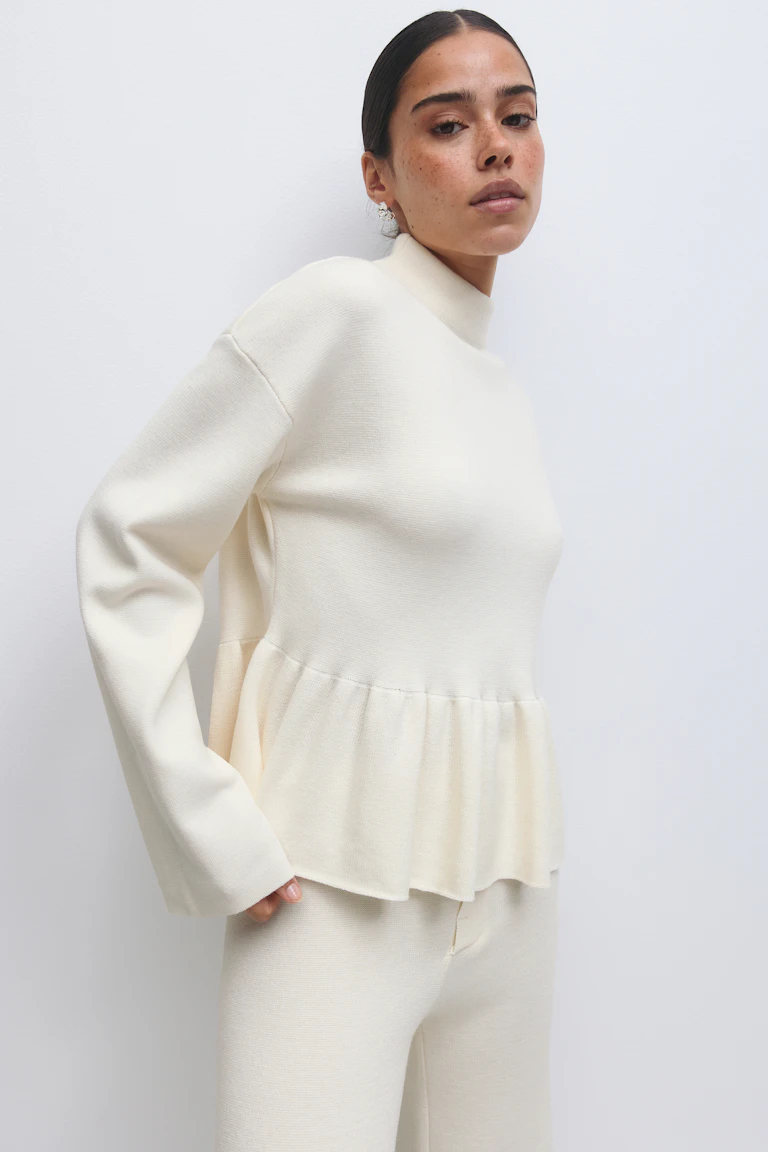Pull en maille crème à col bénitier, manches longues et ourlet péplum, associé à un pantalon en maille crème assorti.