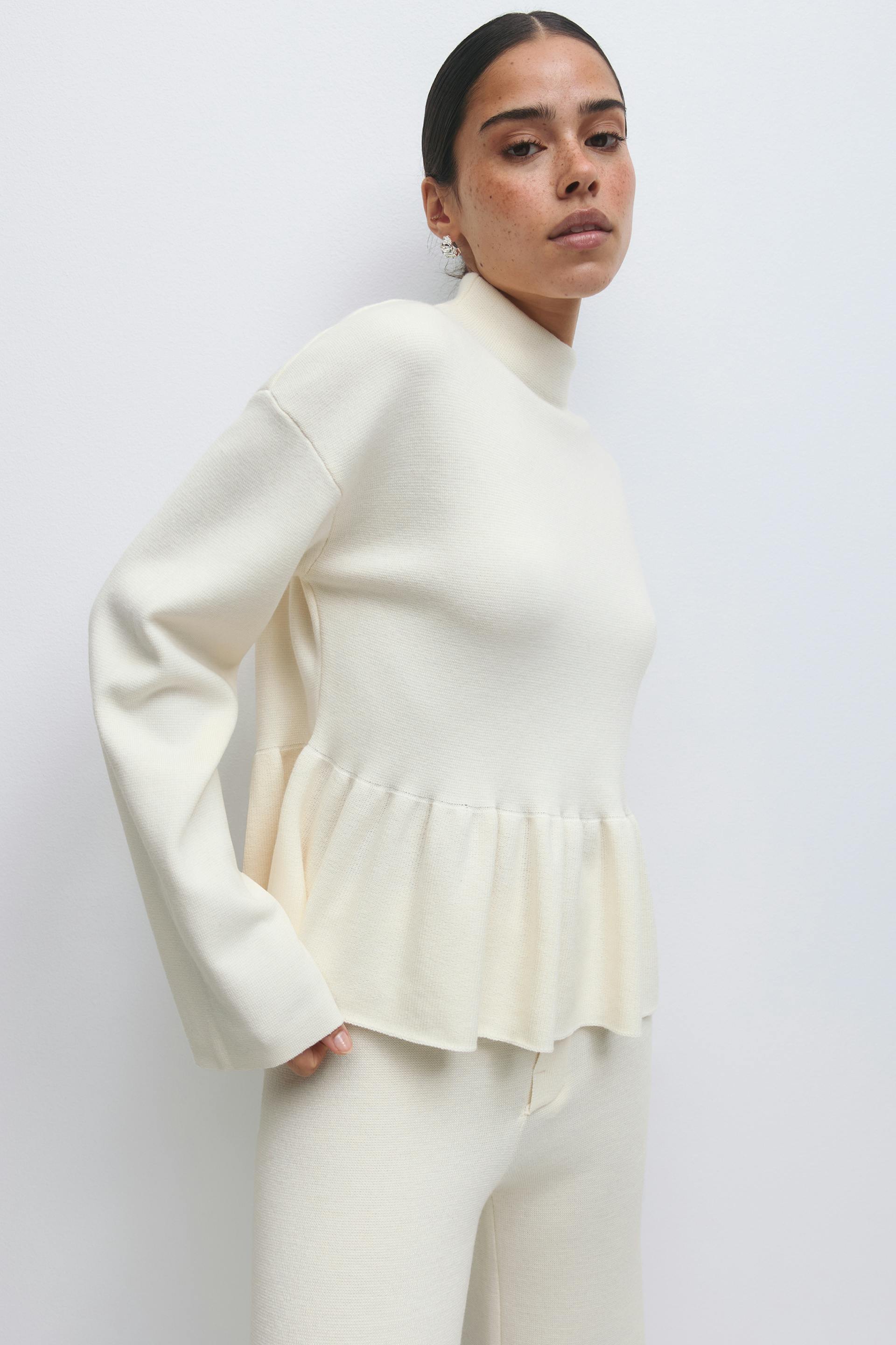 Crème gebreide mock-hals trui met lange mouwen en peplum zoom, gecombineerd met bijpassende crème gebreide broek.