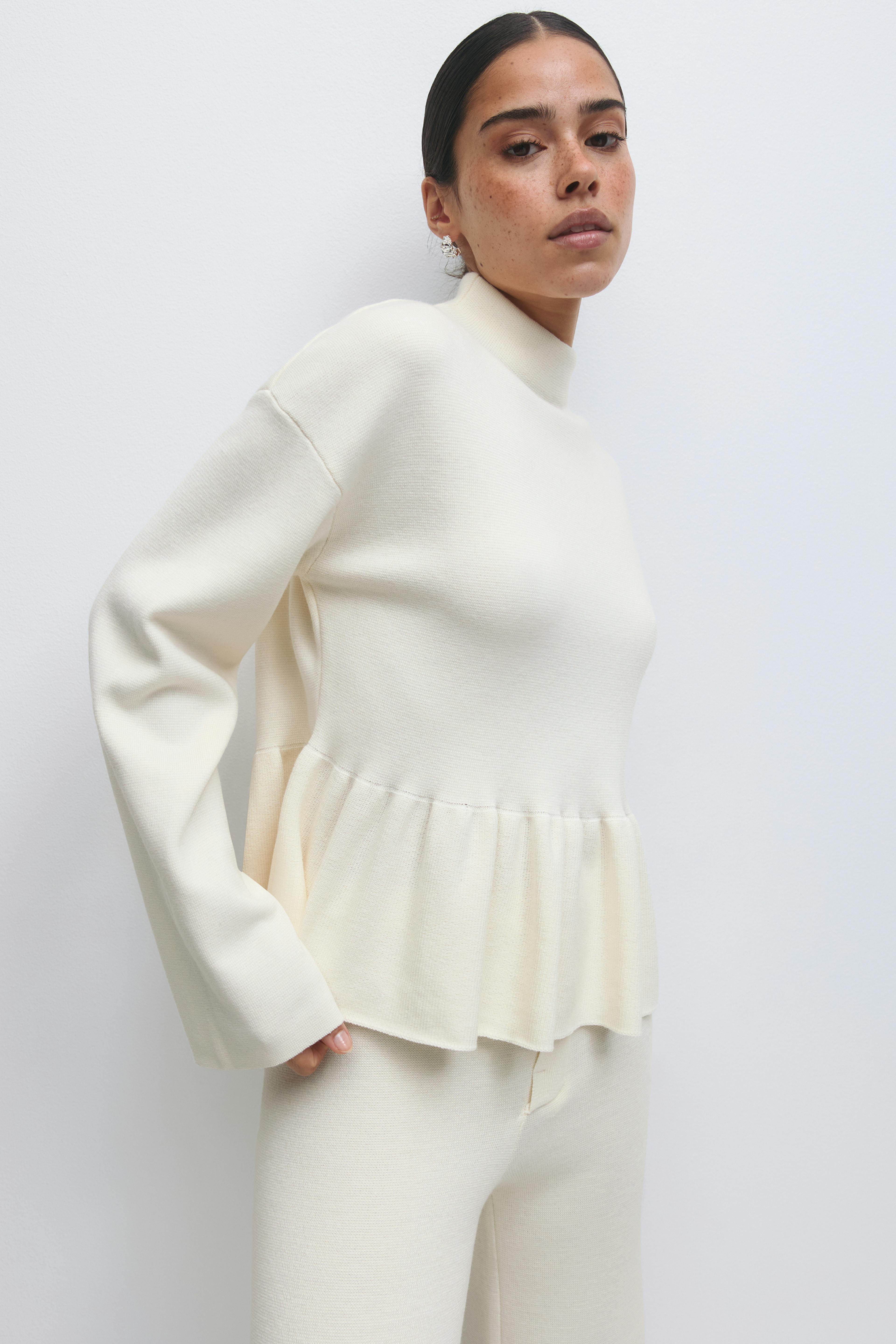 Kermanvärinen neulepusero, jossa on pitkät hihat ja peplum-helma, yhdistettynä yhteensopiviin kermanvärisiin neulehousuihin.