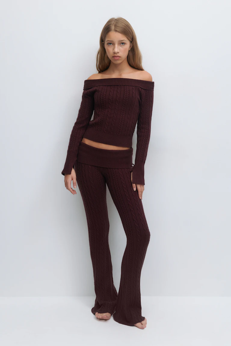 Schulterfreier Pullover aus bordeauxfarbenem Zopfstrick mit langen Ärmeln und geripptem Saum, kombiniert mit einer passenden Schlaghose aus Zopfstrick in hoher Taille.