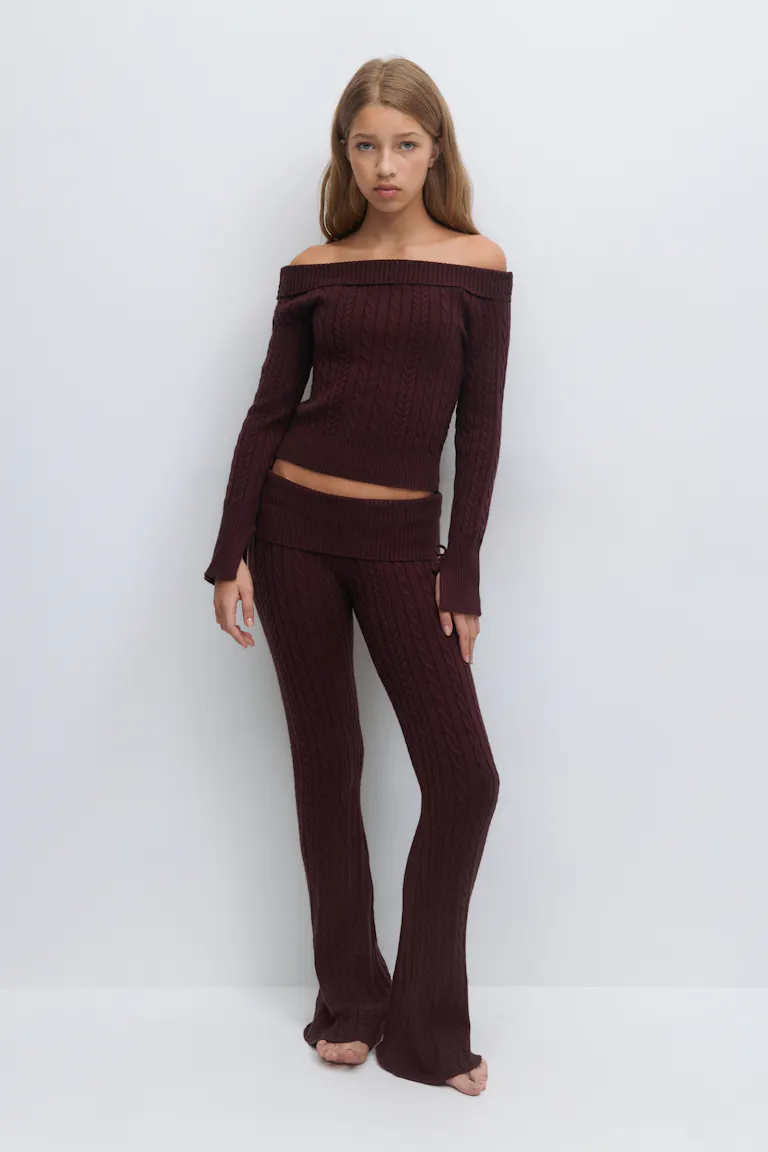 Schulterfreier Pullover aus bordeauxfarbenem Zopfstrick mit langen Ärmeln und geripptem Saum, kombiniert mit einer passenden Schlaghose aus Zopfstrick in hoher Taille.