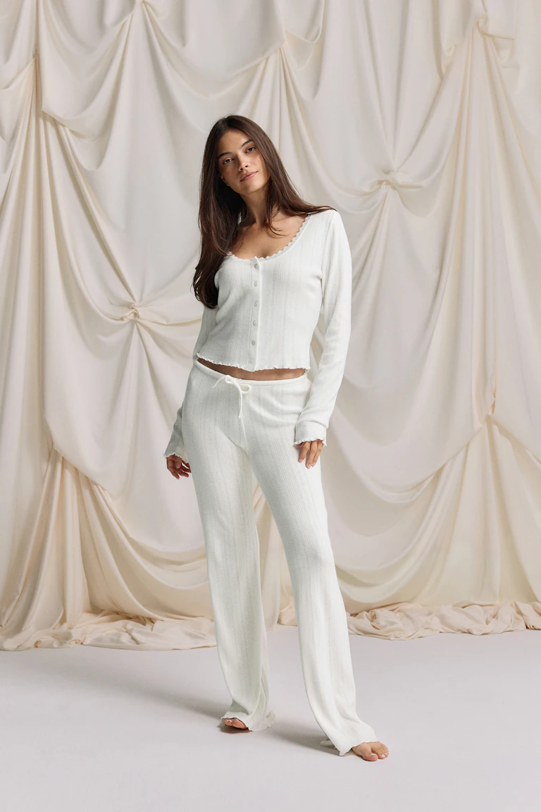 Off-white knit two-piece: a spaghetti-strap camisole with square neckline, front tie and ruffle hem, paired with matching drawstring wide-leg knit trousers with scalloped hems.
