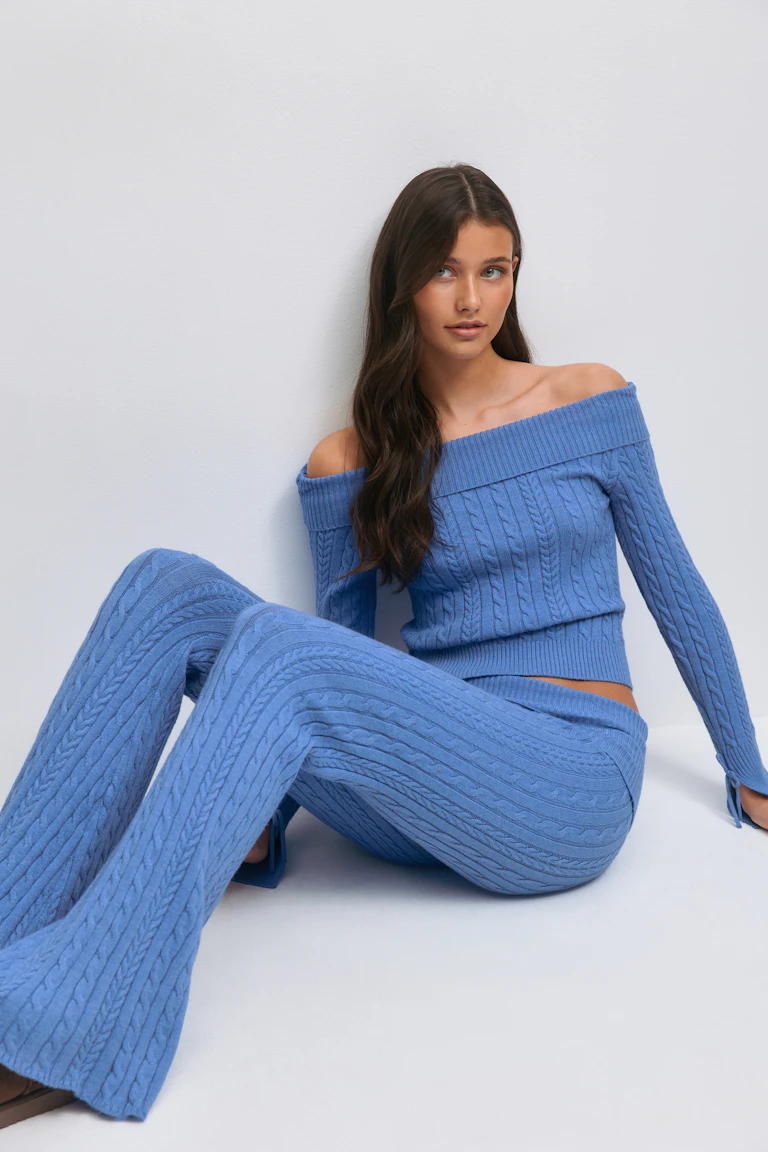 Hellblauer, schulterfreier, langärmeliger Pullover aus Zopfstrick, gepaart mit einer passenden, hochtaillierten Schlaghose aus Zopfstrick.