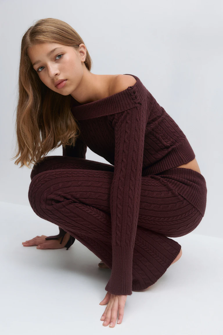 Vinröd kabelstickad off-the-shoulder långärmad croppad tröja kombinerad med matchande kabelstickade utsvängda byxor.