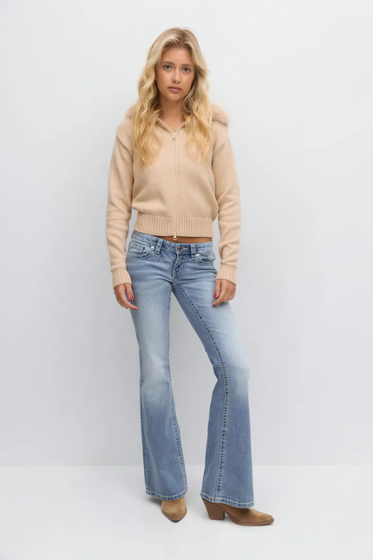 Beige gebreide hoodie met rits, geribde manchetten en zoom en capuchon met imitatiebont; lichtgekleurde flared jeans; tan suède enkellaarsjes met hak.