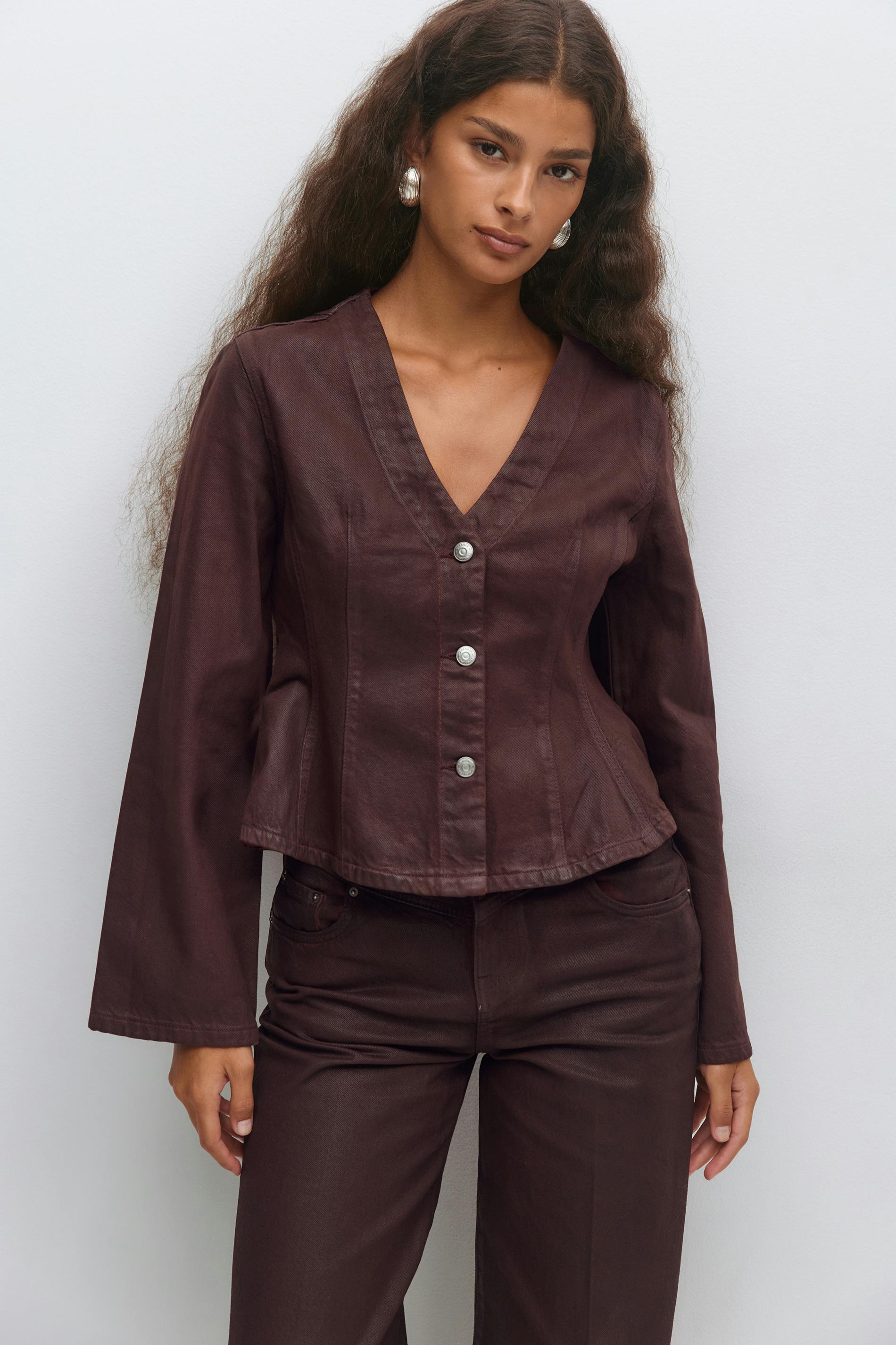 Syvän viininpunainen V-pääntie napitettu takki, jossa on pitkät hihat ja hienovarainen peplum-helma, yhdistettynä yhteensopiviin suoralahkeisiin housuihin; koristeena suuret hopeiset vanne-korvakorut.