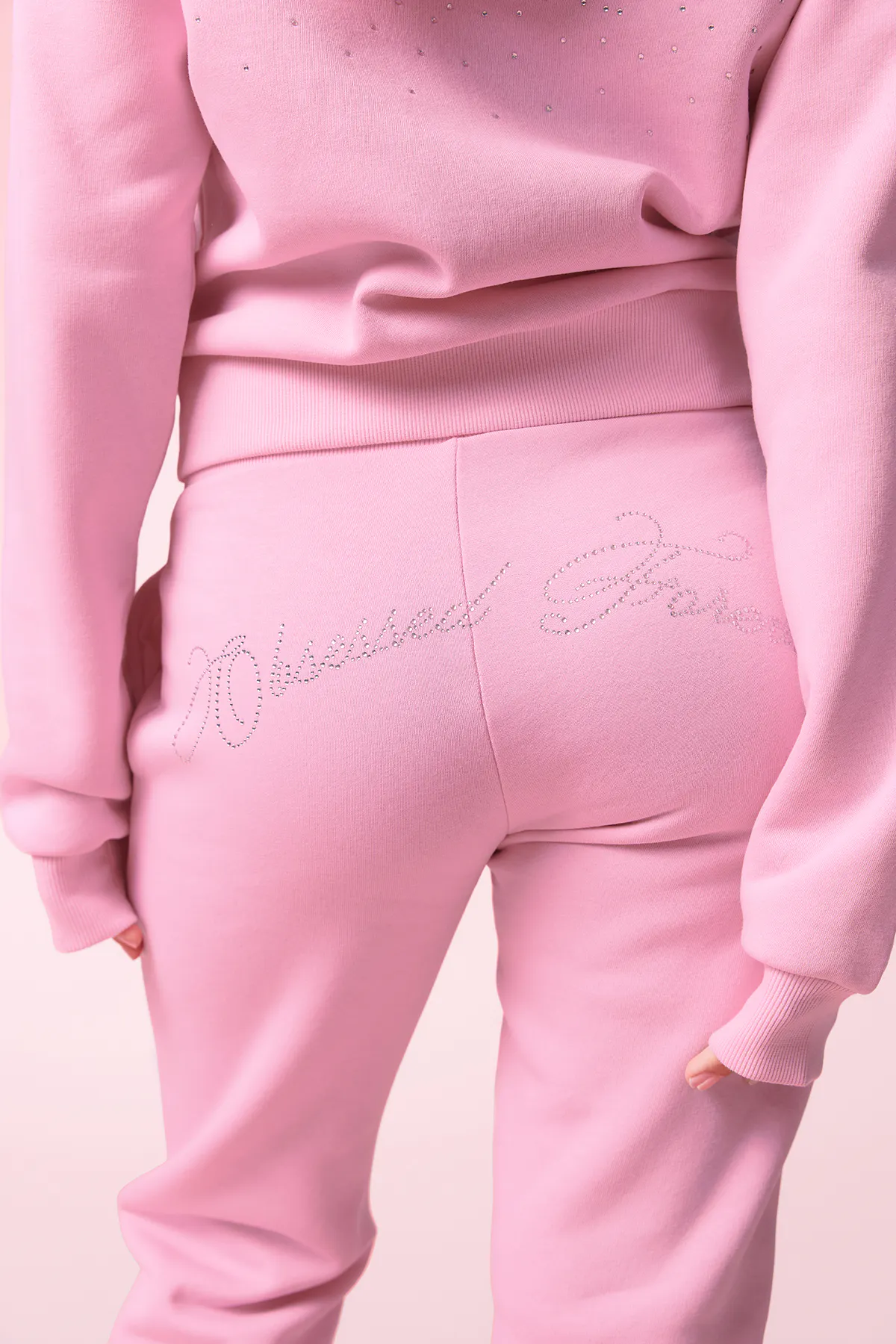 Roze sweater en bijpassende joggersweatpants met geribde tailleband en cursief schrift met kristallen op de achterkant.