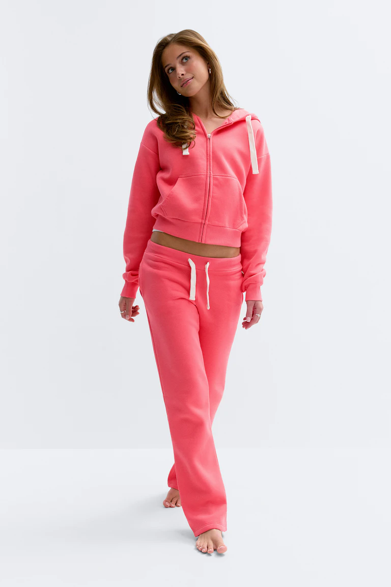 Bijgesneden koraalroze sweater met capuchon en witte trekkoorden en bijpassende koraalroze joggingbroek met trekkoord.