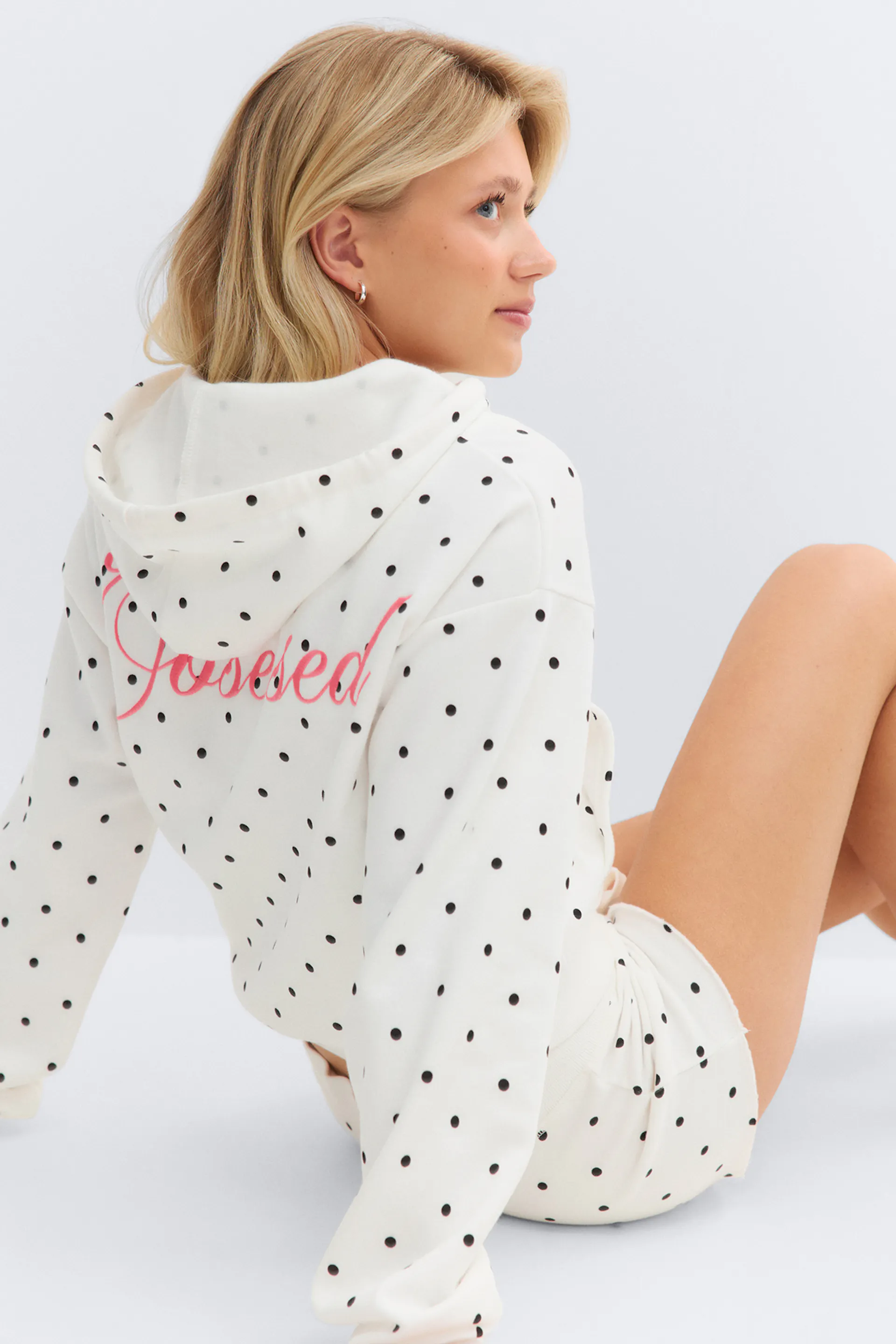 Sweat à capuche blanc à pois noirs et écriture rose dans le dos, associé à un short à pois blancs assorti.
