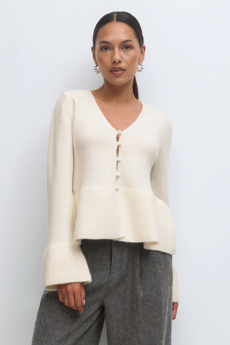 Cremefarvet peplum-cardigan med V-udskæring og knap foran og ribbede manchetter i overstørrelse, sat sammen med højtaljede grå sildebensbukser.
