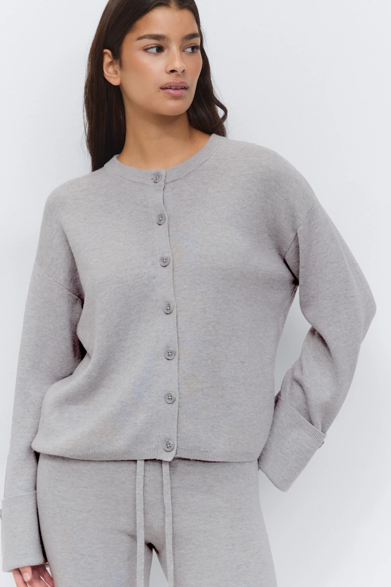 Lichtgrijs gebreid vest met knoopsluiting, ronde hals en lange mouwen, gecombineerd met een bijpassende lichtgrijze gebreide broek met koord.