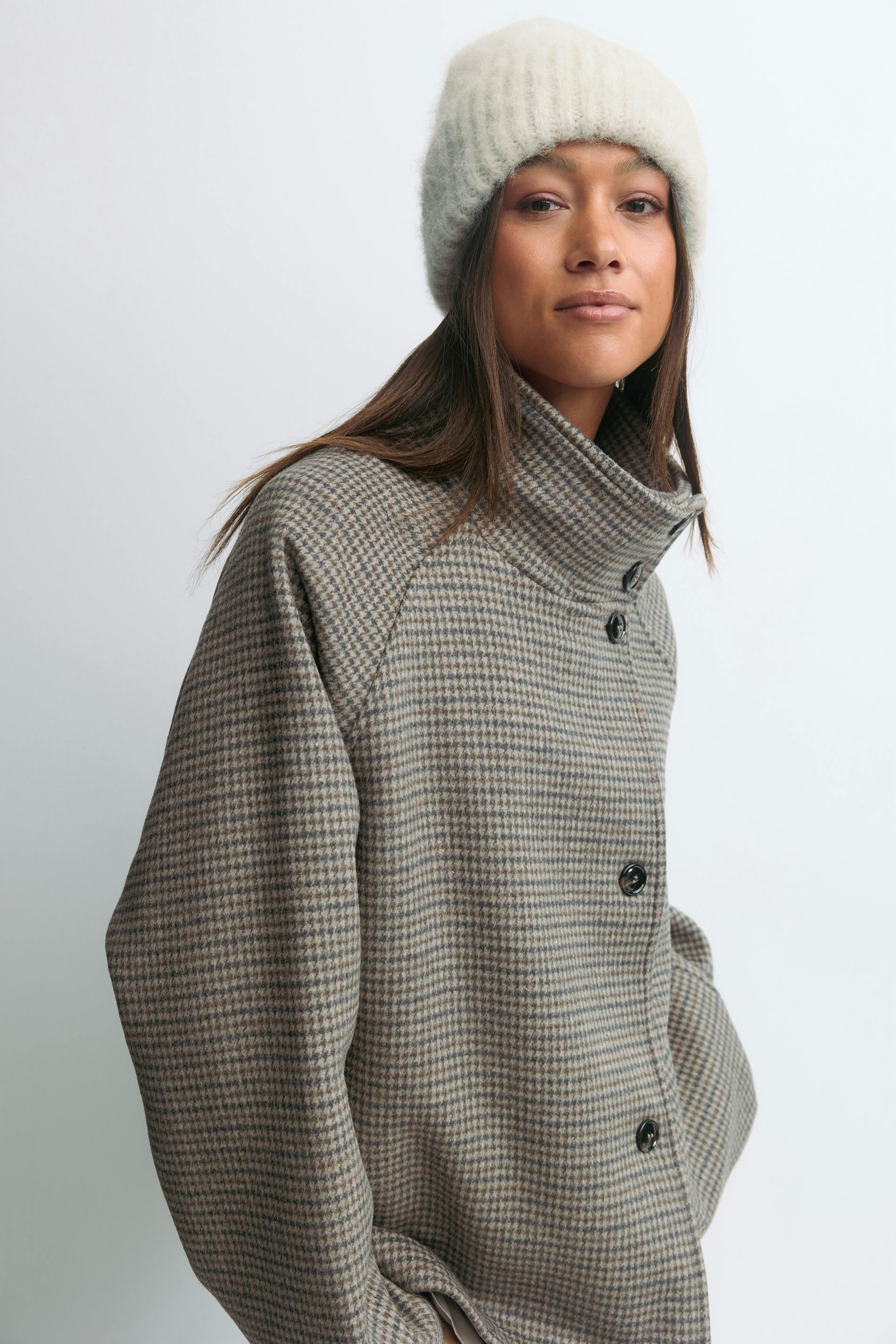 Krämfärgad ribbstickad mössa och taupe- och gråfärgad liten houndstooth-kappa med hög krage och svarta knappar.