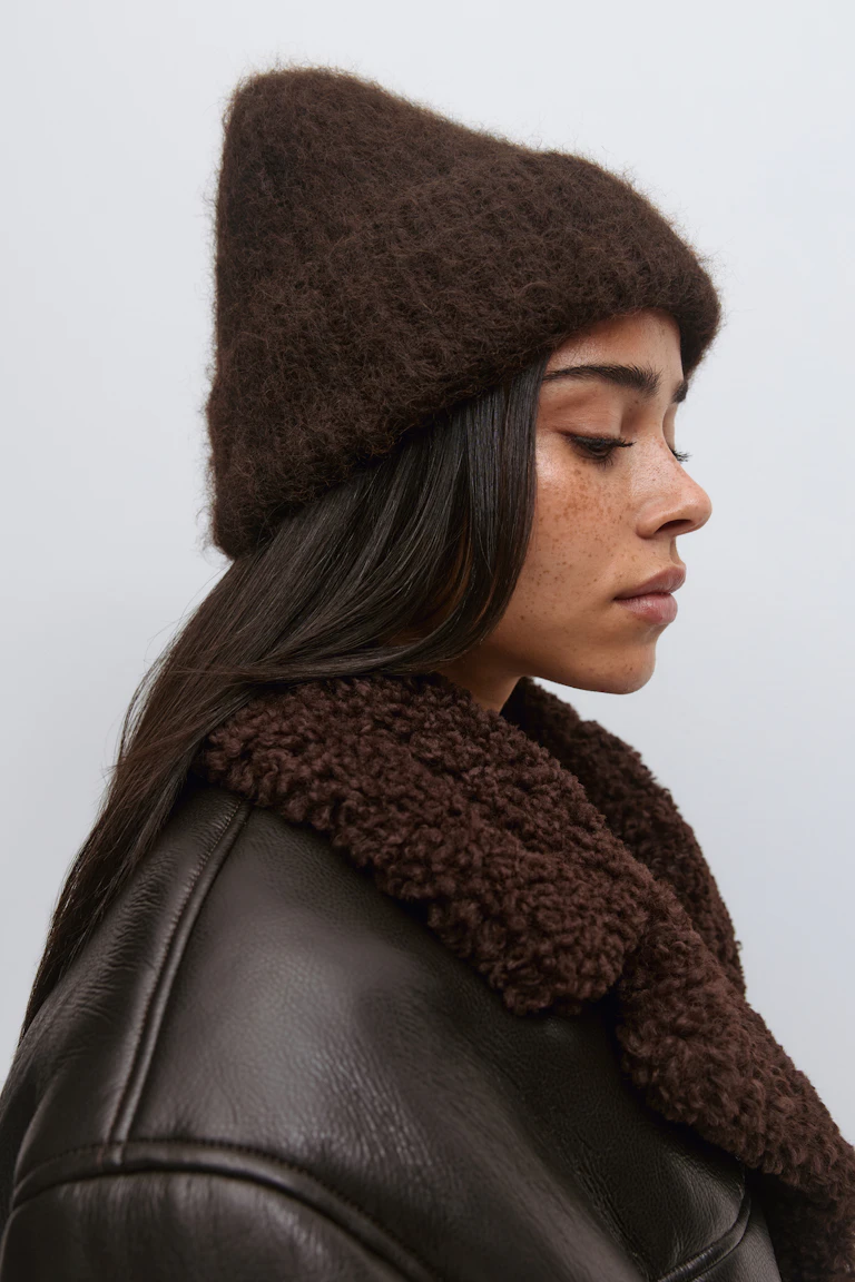 Dunkelbraune, flauschige Strickmütze und passende dunkelbraune Lederjacke mit strukturiertem Shearling-Kragen.