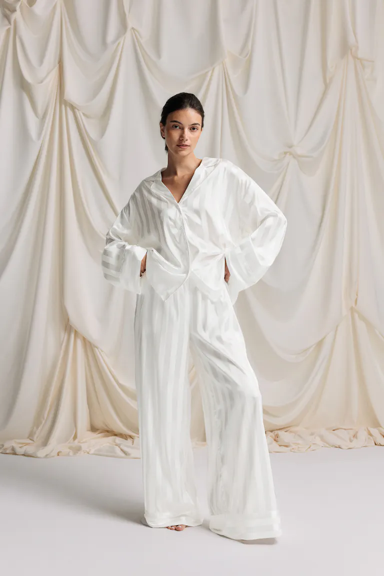 Pyjamaset in wit satijn met ton-sur-ton strepen: oversized button-down overhemd met lange mouwen en ingekeepte kraag en bijpassende broek met wijde pijpen.
