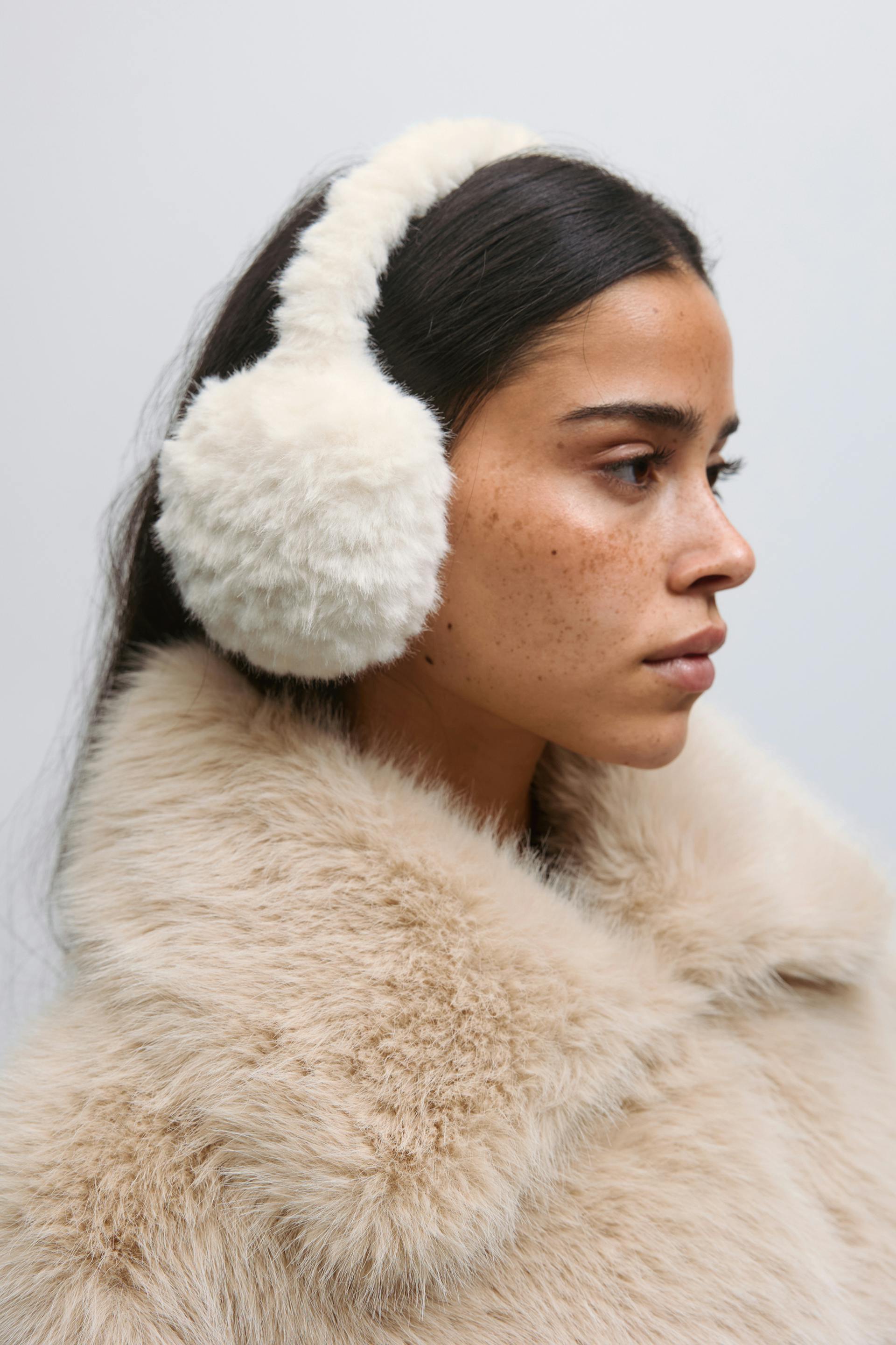 Cream faux‑fur earmuffs paired with a light beige faux‑fur coat featuring a voluminous collar.