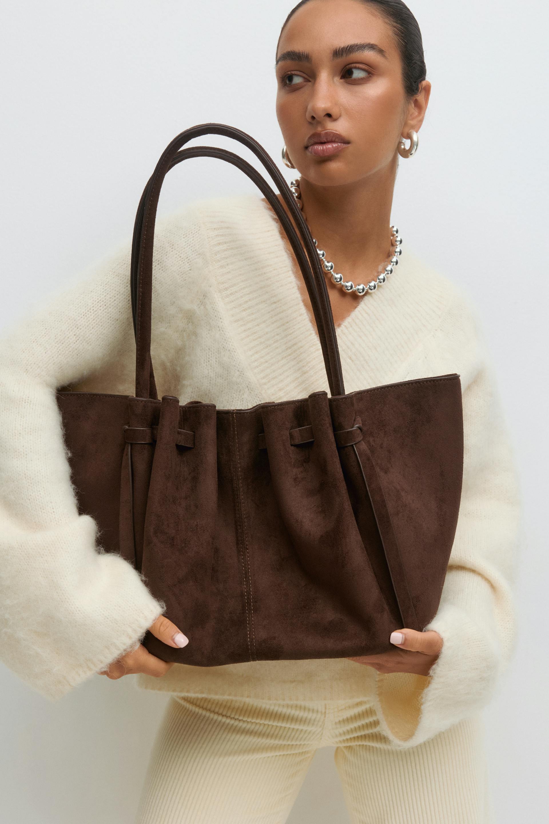 Ivory mohair V-neck sweater, ivory ribbed trousers, chunky silver bead necklace, silver hoop earrings, and a large dark-brown suede tote bag with double handles.
