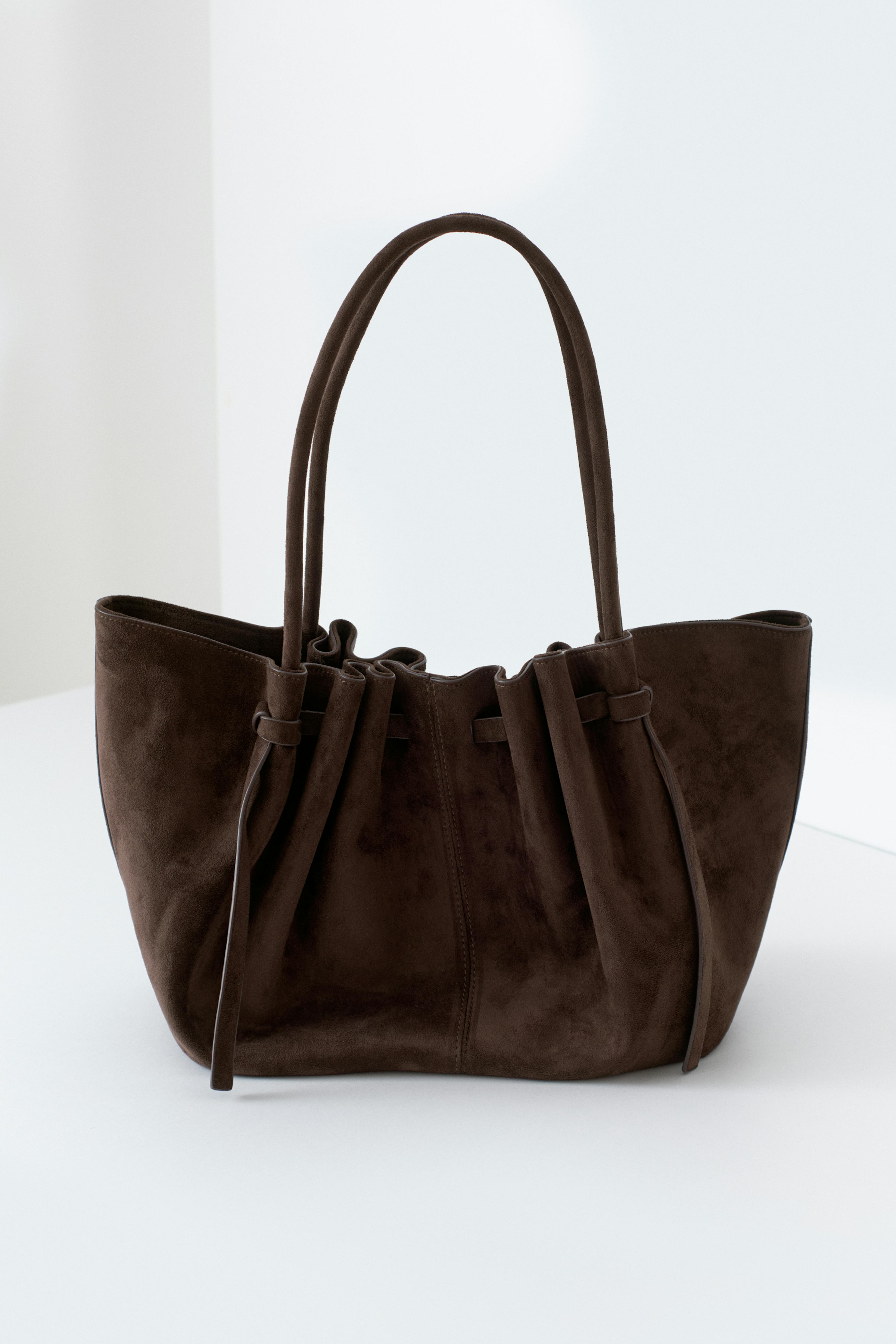 Ivoorkleurige mohair trui met V-hals, ivoorkleurige geribde broek, dikke zilveren kralenketting, zilveren oorbellen en een grote donkerbruine suède tas met dubbele hengsels.