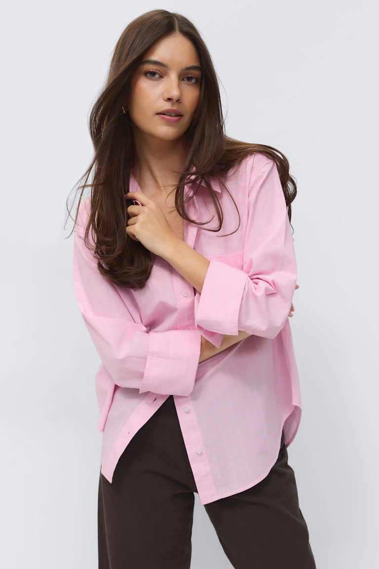 Light pink collared button‑up shirt with rolled sleeves, paired with dark brown trousers.