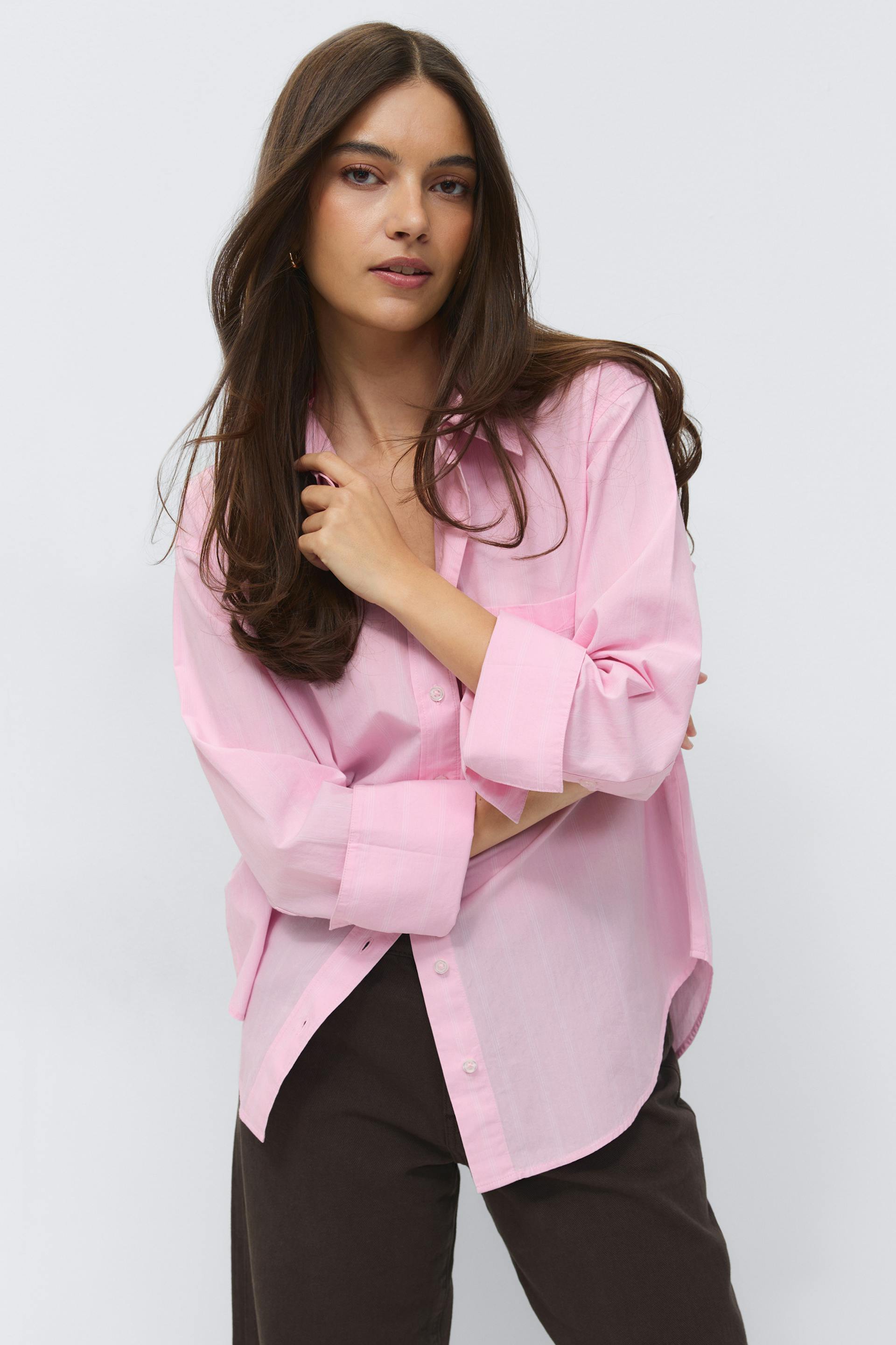 Hellrosa Hemd mit Kragen und gekrempelten Ärmeln, gepaart mit einer dunkelbraunen Hose.