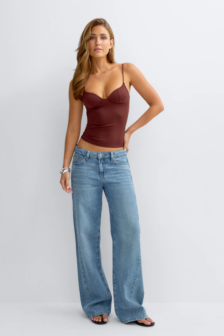 Zwarte gedrapeerde top met lange mouwen, vleermuismouwen en ronde hals, gecombineerd met een lichtblauwe jeans met hoge taille en wijde pijpen en zwarte platte schoenen.