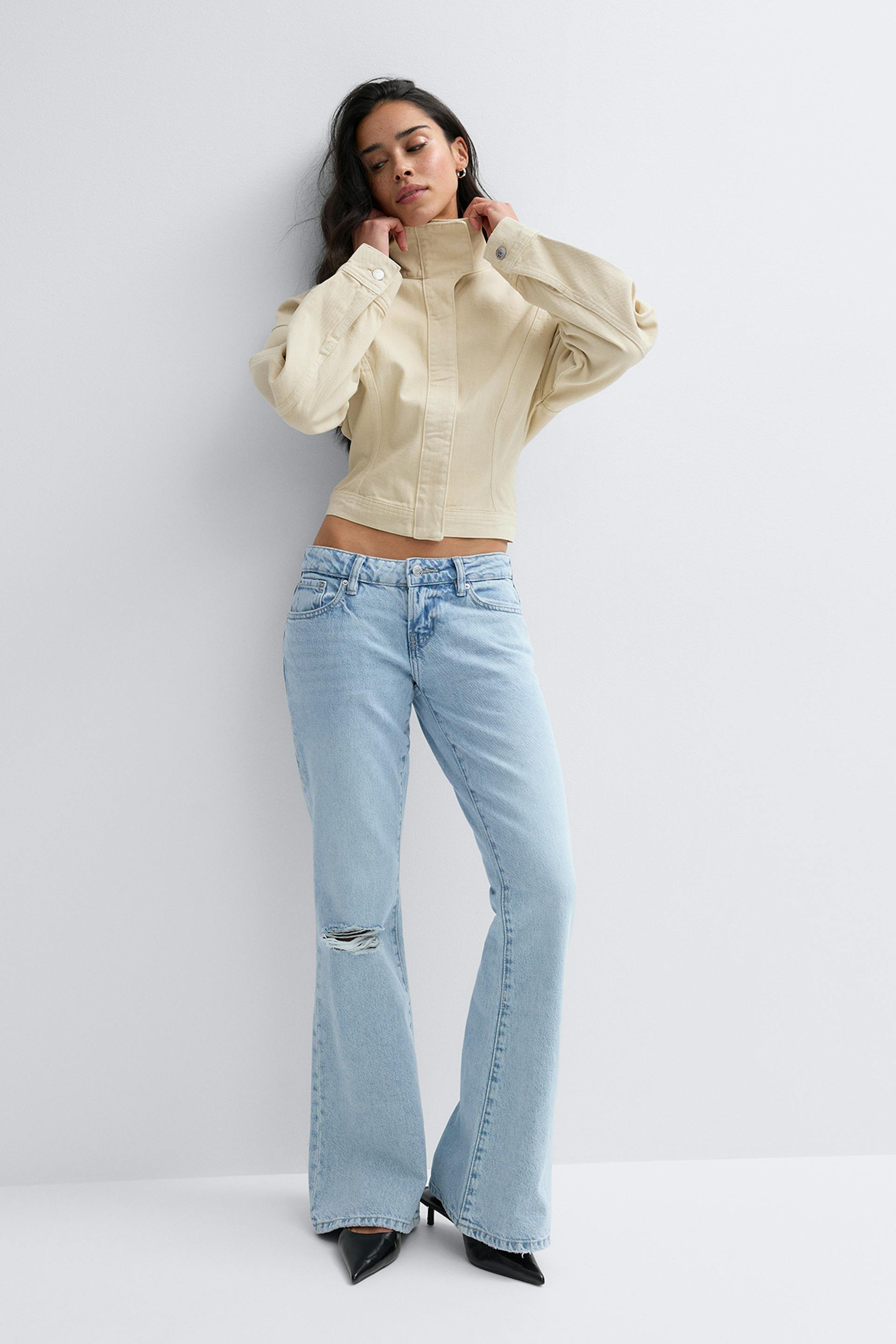 Beigeinen, korkeakauluksinen, pitkillä, tuuheilla hihoilla ja napitetuilla hihansuilla varustettu cropped-takki, johon on yhdistetty vaaleat, korkeavyötäröiset, levenevät farkut, joissa on polvivaurioitunut polvi, ja mustat teräväkärkiset korkokengät.