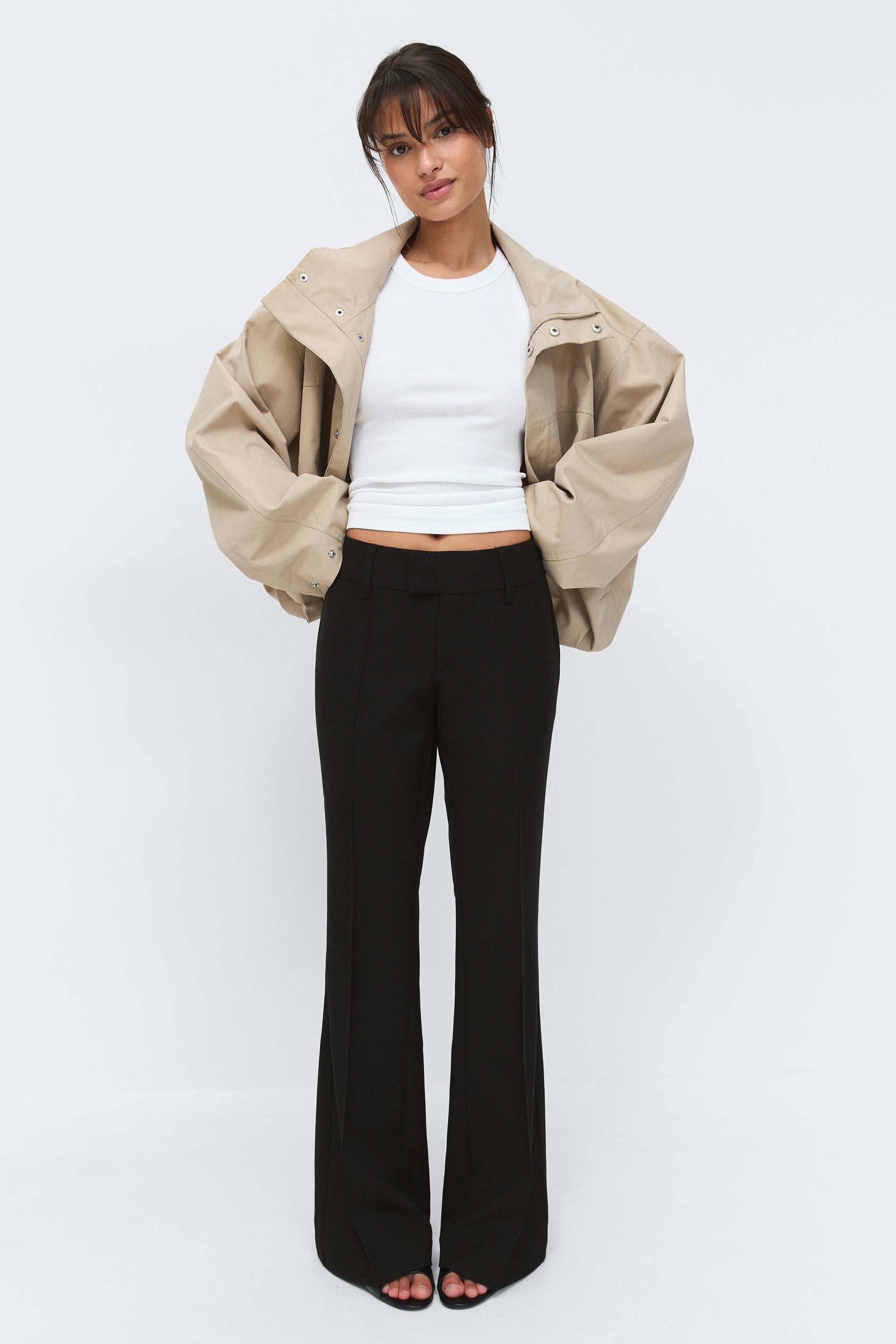 Beige oversized snap-front jacket over a white ribbed sleeveless crop top, paired with black high‑waisted tailored flared trousers and black open‑toe heels.