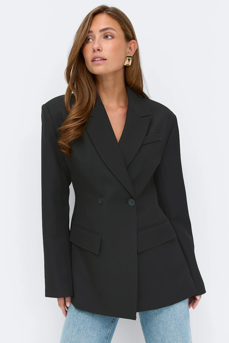 Zwart getailleerd colbert met dubbele revers, tweeknoopssluiting, klepzakken en lange mouwen, gestyled met een lichtblauwe spijkerbroek en gouden geometrische oorbellen.