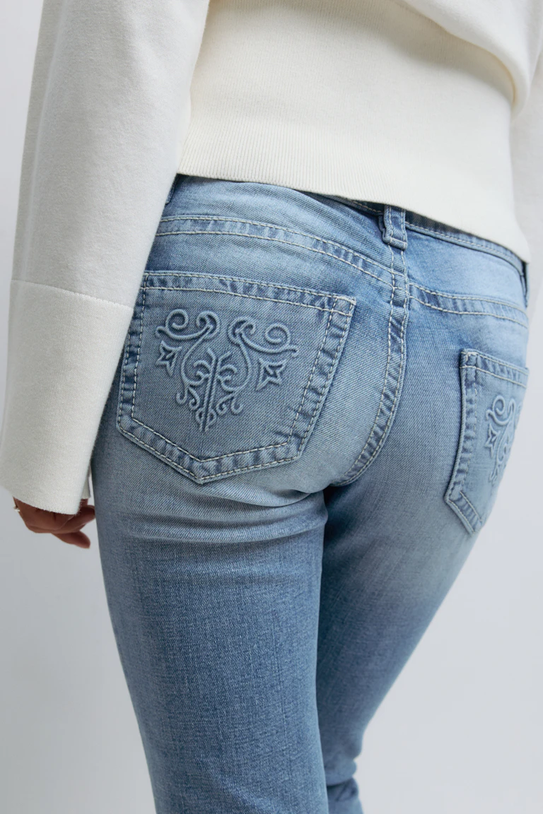 Vit långärmad tröja tillsammans med lätt tvättade blå jeans med broderade bakfickor.