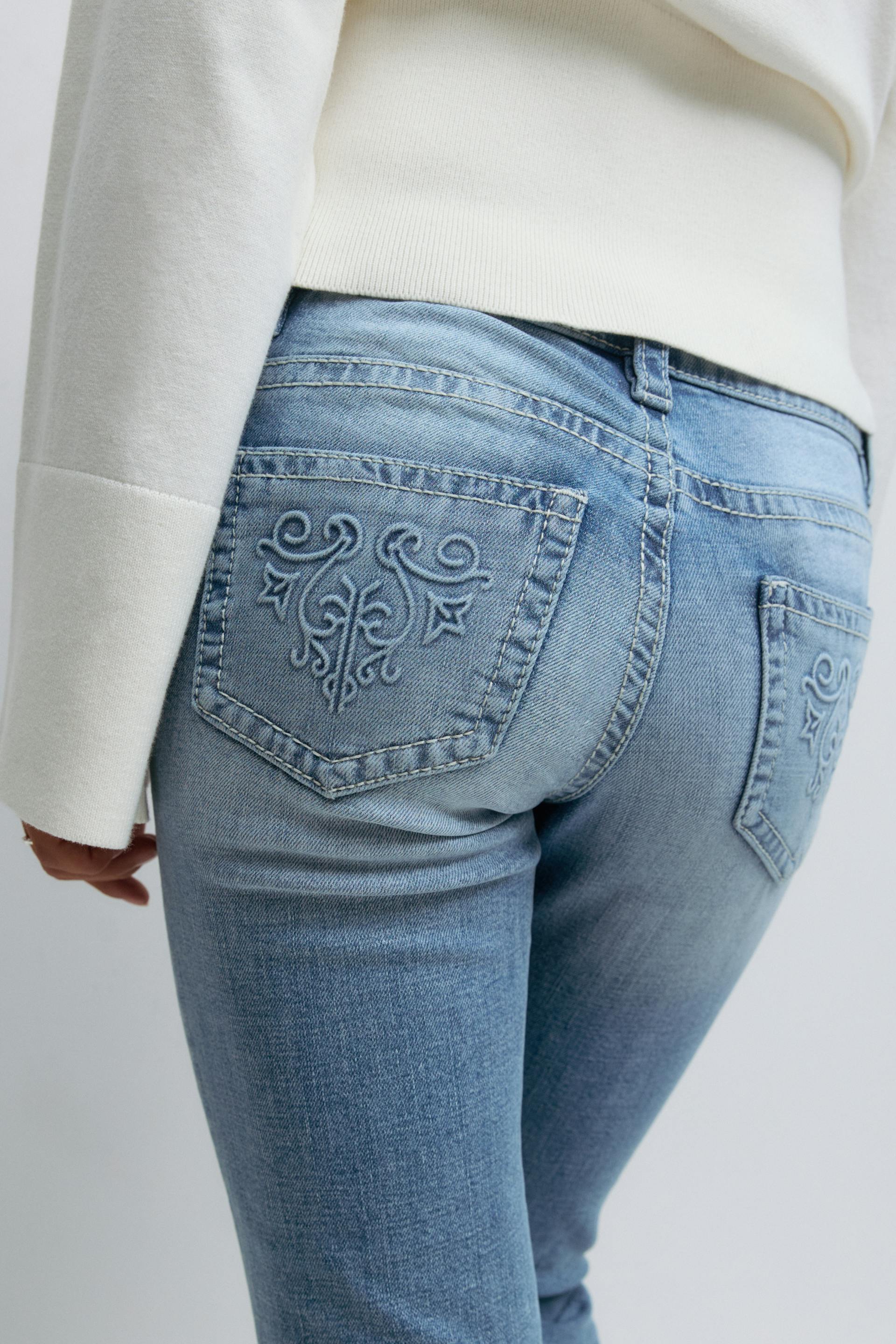 White long-sleeve sweater paired with light-wash blue jeans featuring embroidered back pockets.
